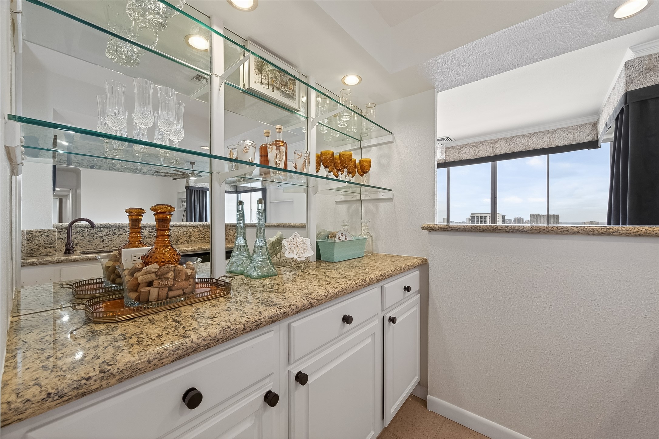 Elegant wet bar with sleek granite countertops, ample cabinet storage, and glass shelves displaying crystal glassware, perfect for entertaining.