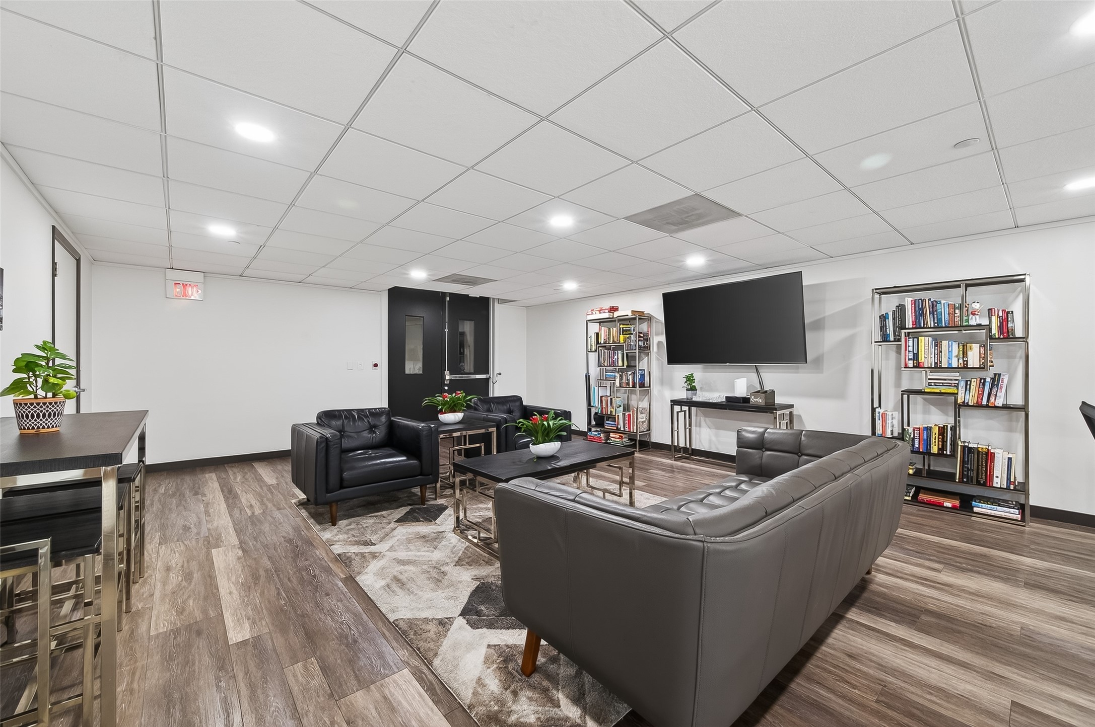 Spacious modern lounge area featuring sleek black leather seating, a large wall-mounted TV, stylish bookshelves, and contemporary decor, perfect for relaxation and entertainment.