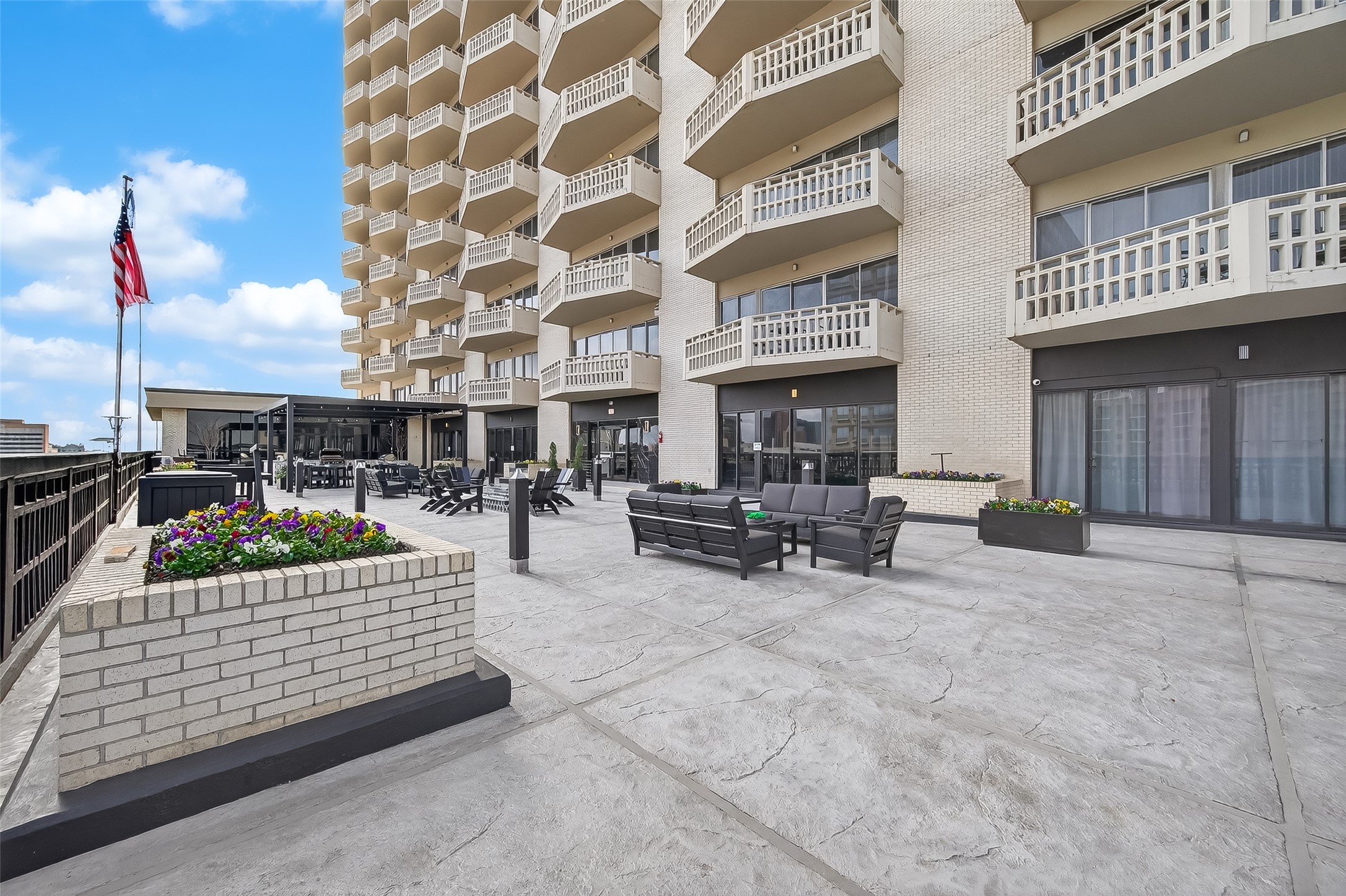 Expansive terrace with comfortable seating and vibrant planters, set against a backdrop of a modern building with private balconies.
