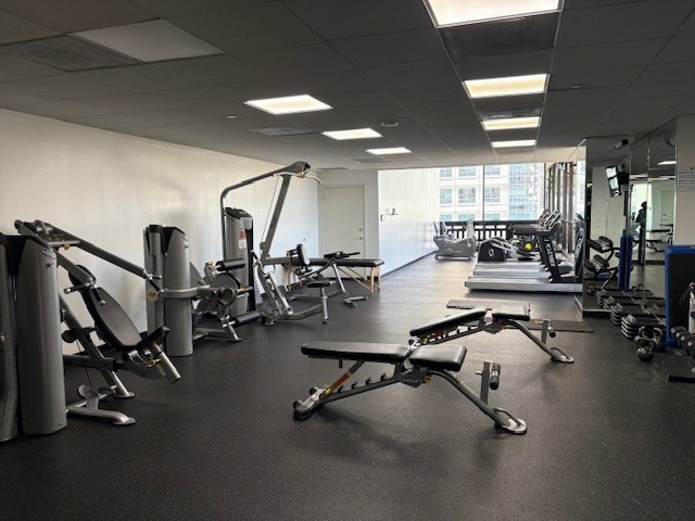Spacious fitness center with modern exercise equipment, including weight machines, benches, and treadmills, all set in a bright, well-lit area.