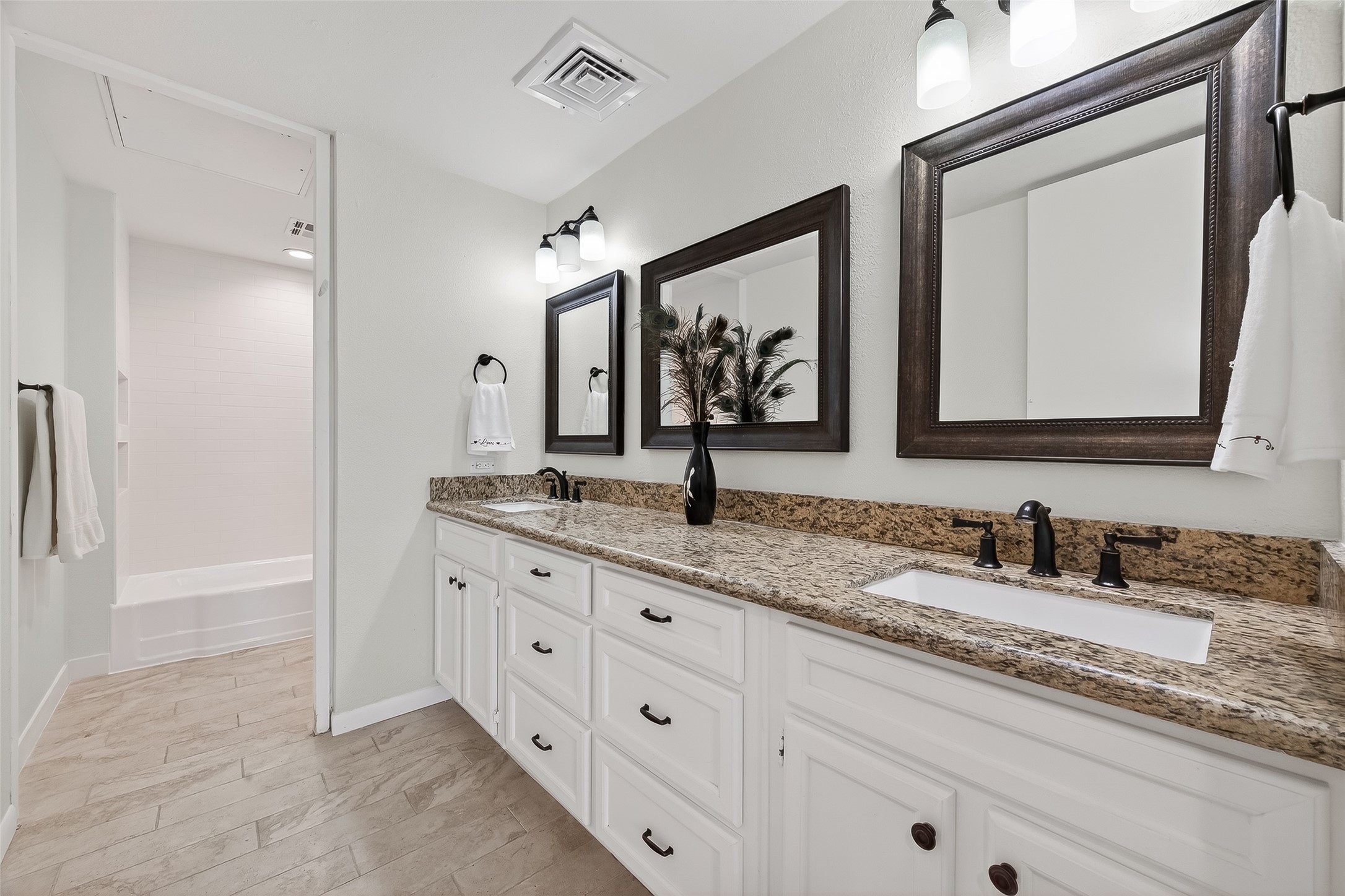 Elegant bathroom featuring a granite double vanity with dark fixtures, complemented by framed mirrors and sleek lighting.
