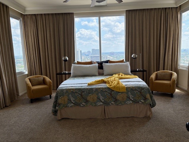 Spacious bedroom with panoramic city views, featuring a cozy bed adorned with a decorative throw, flanked by elegant armchairs and floor-length drapes.