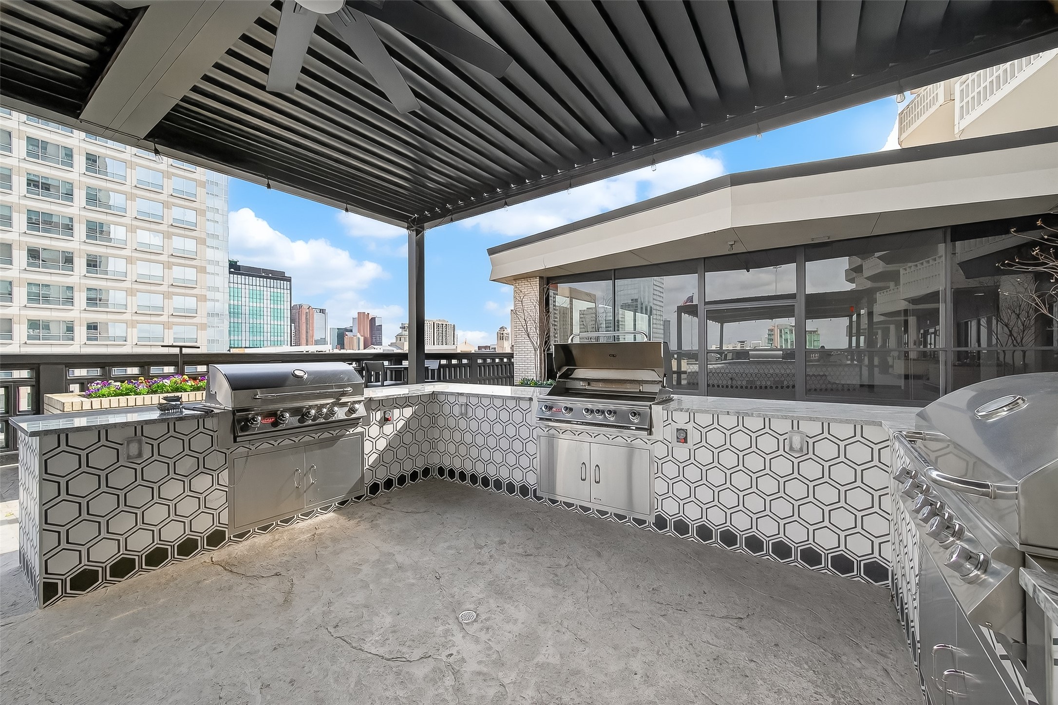 Experience luxury outdoor living with this stylish rooftop terrace featuring a sleek built-in grill station, modern hexagon tile accents, and expansive city views. Perfect for entertaining.