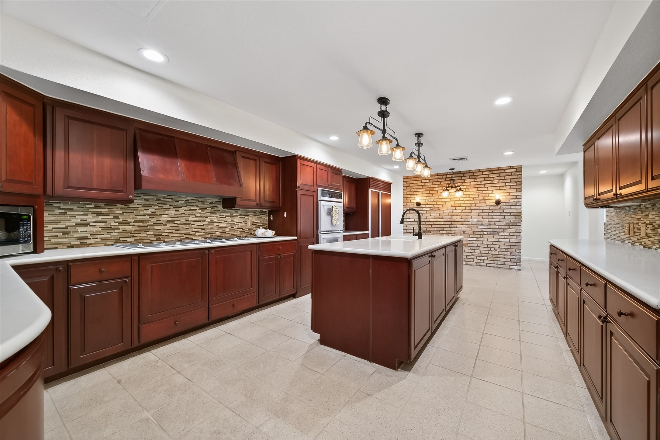 Spacious kitchen featuring rich wood cabinetry, a large central island with modern lighting, and elegant tile backsplash, perfect for culinary enthusiasts.