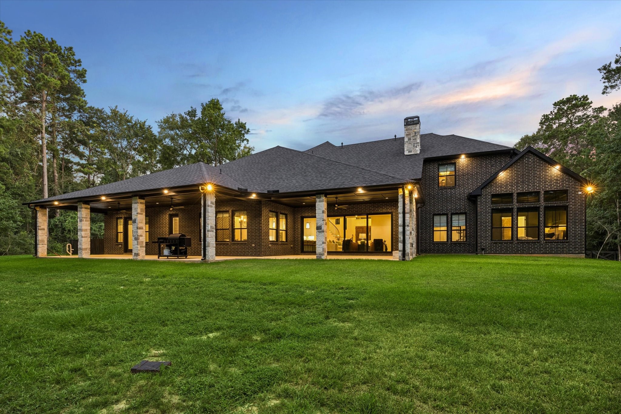As dusk settles, the rear elevation reveals the home's impressive architectural presence. Expansive covered living areas, beautifully landscaped grounds, and timeless design create a private estate equally suited for intimate evenings or grand celebrations.