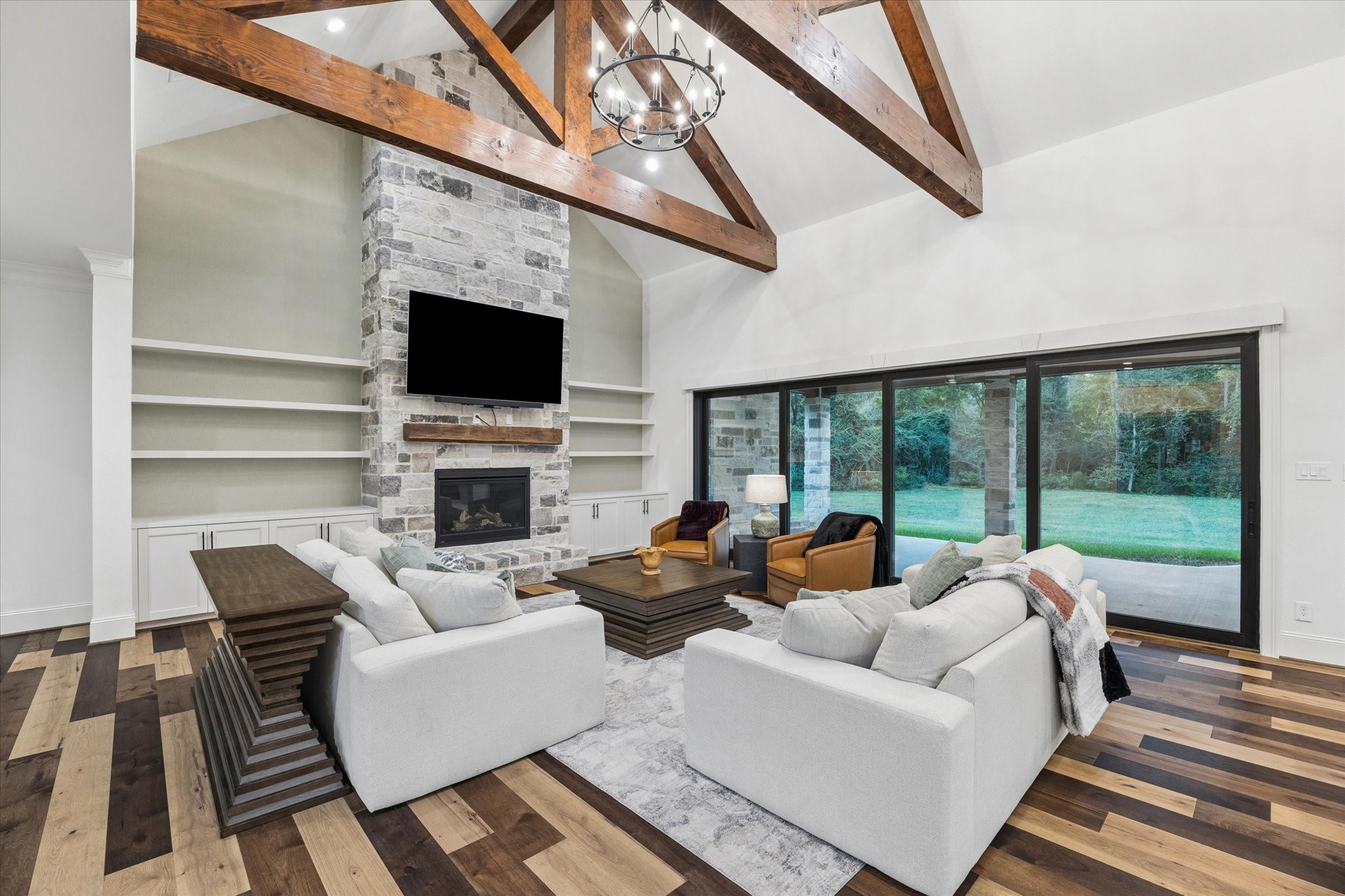 The great room is the heart of the home, where soaring vaulted ceilings and exposed wood trusses create a stunning architectural statement. A sophisticated linen-texture accent wall beautifully complements the custom-built shelving, adding warmth and designer appeal. Walls of glass fill the space with natural light, while the open layout seamlessly blends luxury, comfort, and timeless eleganceperfect for both entertaining and everyday living.
