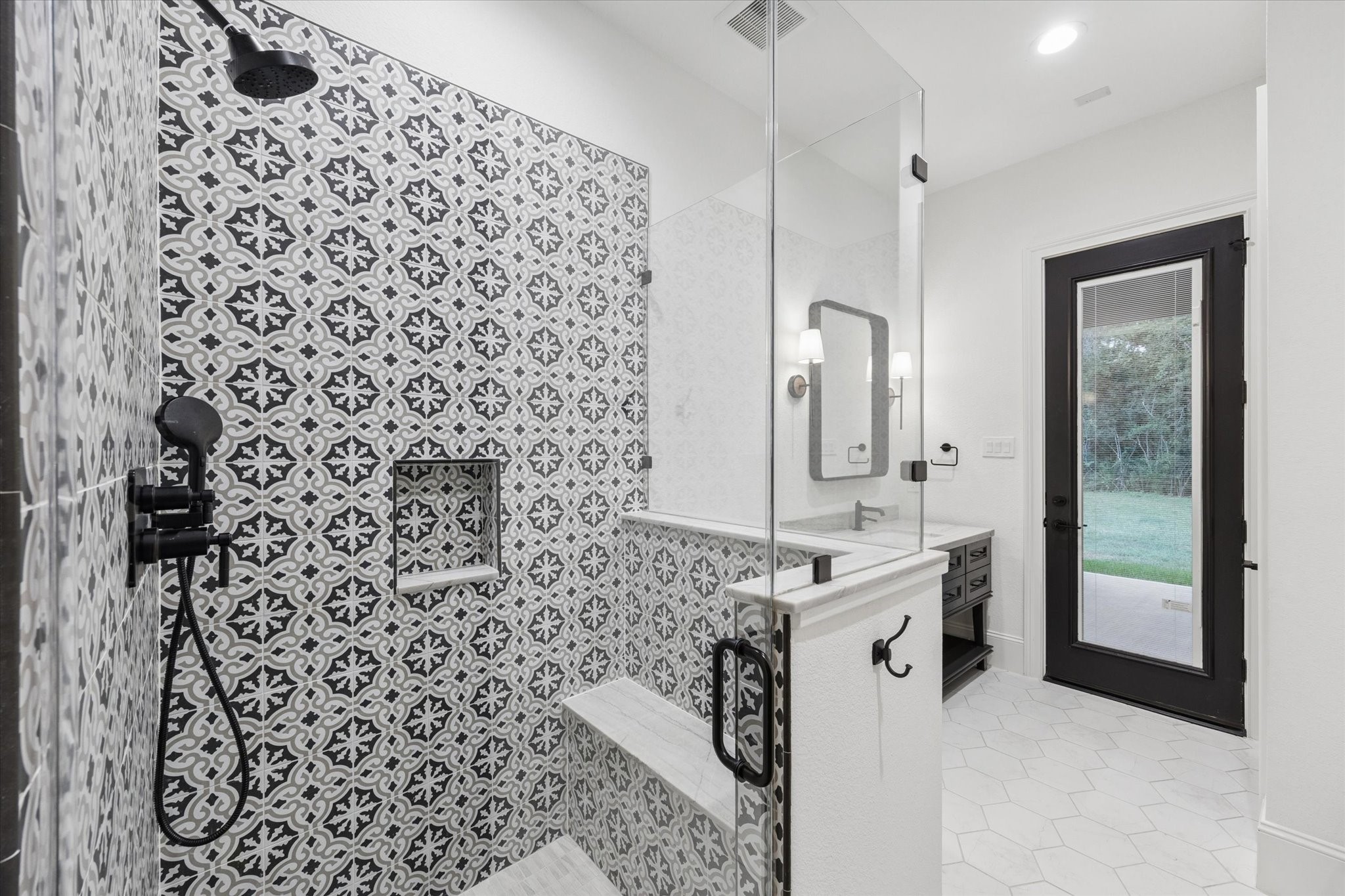 The full pool bathroom provides convenient access from both the interior and the covered patio, making it ideal for future pool use and outdoor entertaining. A striking patterned shower wall creates a dramatic designer focal point, while the walk-in shower includes built-in niches and carefully selected fixtures. Clean architectural lines, abundant natural light, and direct exterior access combine style and practicality in a space thoughtfully designed to support the homes indoor-outdoor lifestyle.