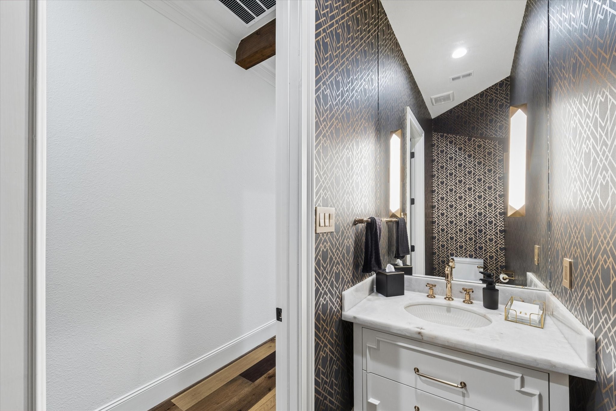 The dramatic powder bath makes a memorable impression with its sophisticated jewel-box design. Full custom wallpaper surrounds the space with rich pattern and dimension, while a floating custom vanity topped with marble adds modern elegance. A full-height mirror extending toward the ceiling, designer sconces, and thoughtfully coordinated finishes create a refined guest experience. Every element reflects the homes commitment to distinctive materials and elevated craftsmanship.