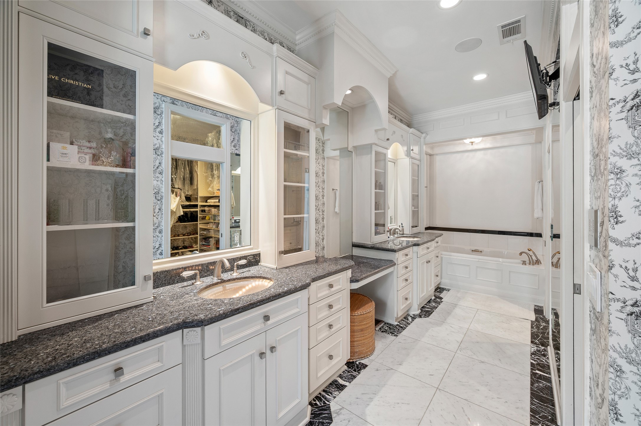 [Primary Bath]
Elegant granite, mirror, and marble finishes enhance the primary bath. Note glass-front upper cabinets, vanity counter, and jetted tu. Interior of the primary closet is reflected in the center mirror.