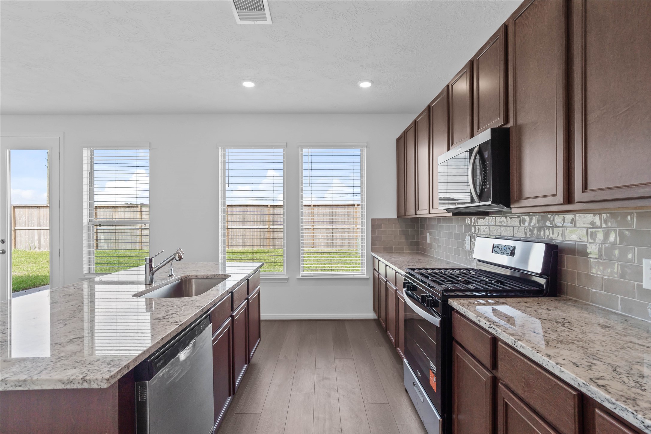 Beautiful view of the kitchen featuring stainless steel appliances, sleek granite countertop, gorgeous Woodmont cabinetry, and modern Daltile backsplash.