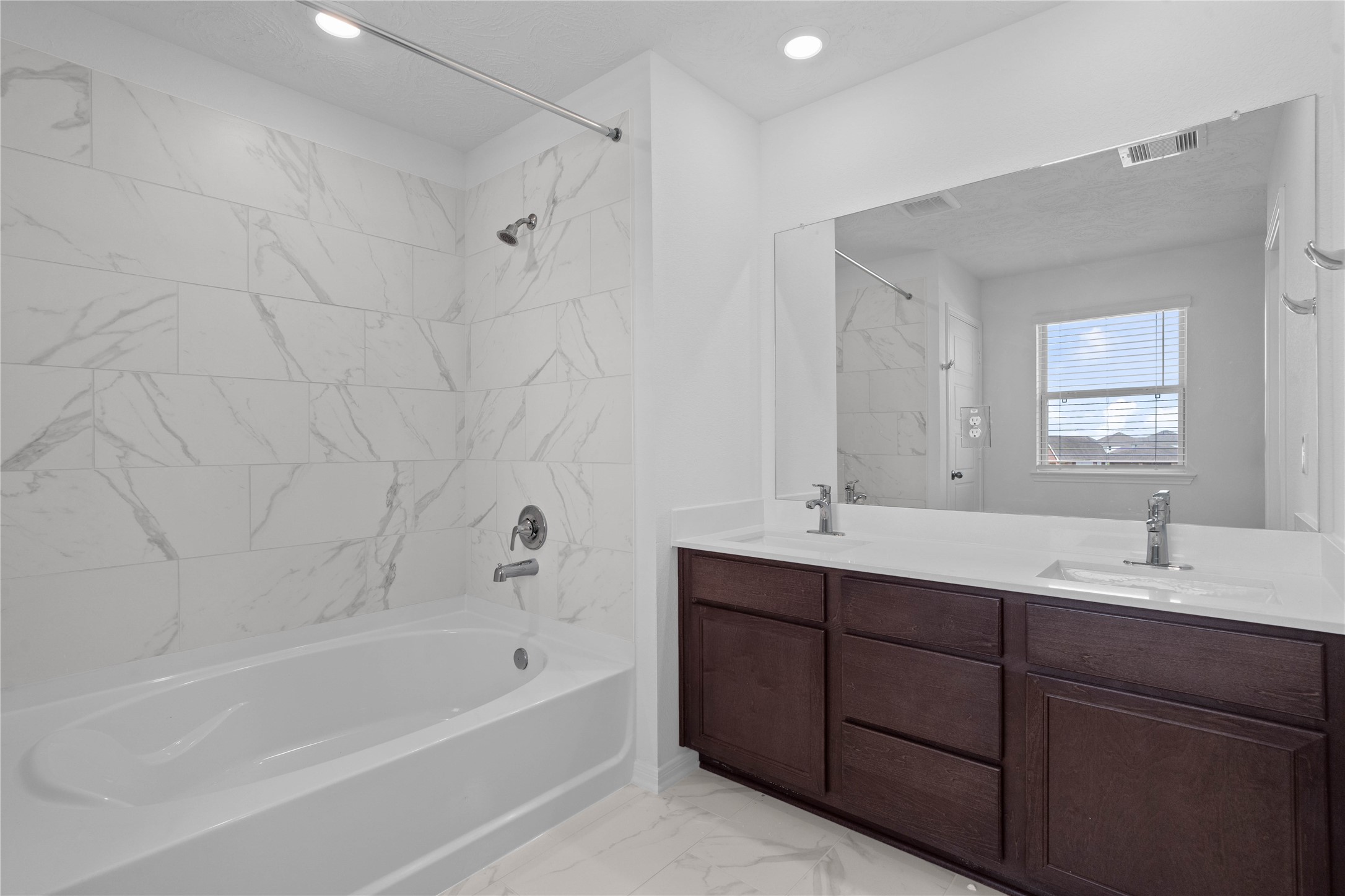 This primary bathroom is definitely move-in ready! Featuring dual sinks, stained cabinets with light countertops, mirror, high ceilings, neutral paint, tub/shower combination with tile surround, sleek fixtures, and modern finishes.