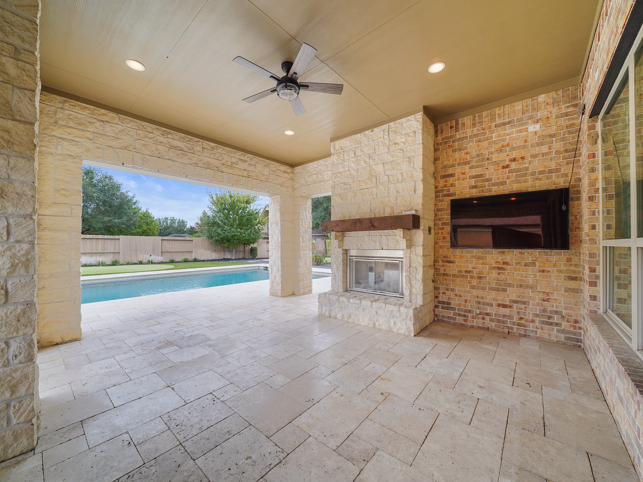 Out back, the covered patio unfolds as an open-air living room, complete with a fireplace and a backdrop of poolside views.