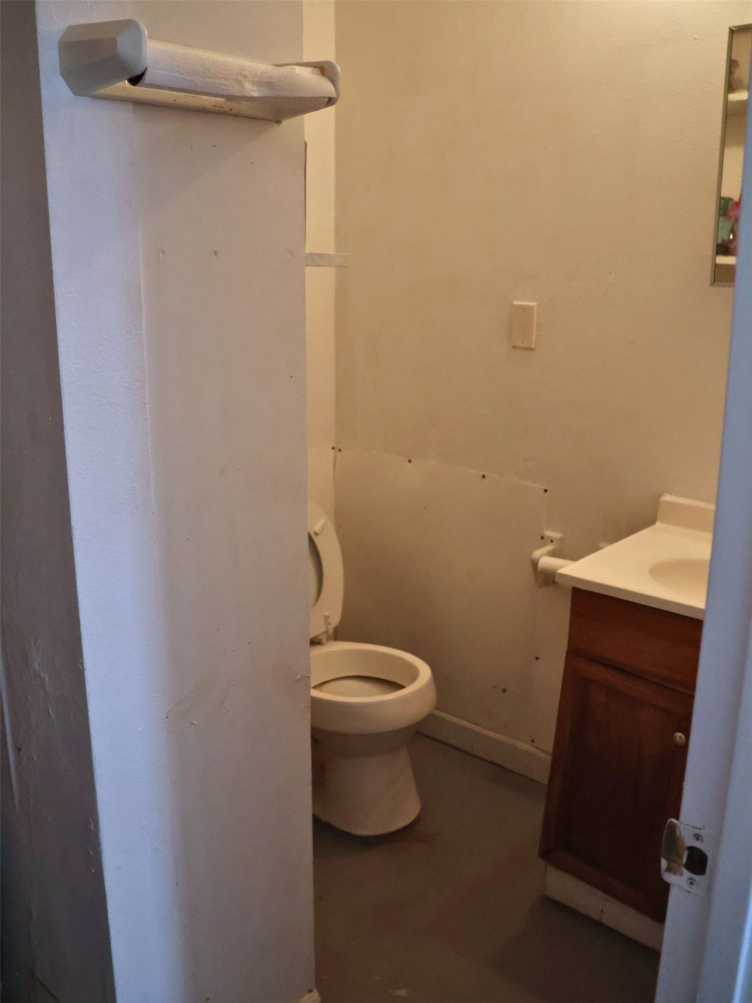 This photo shows a compact bathroom with a toilet, a small vanity with a sink, and a towel rack. The space appears basic and might benefit from some updates.