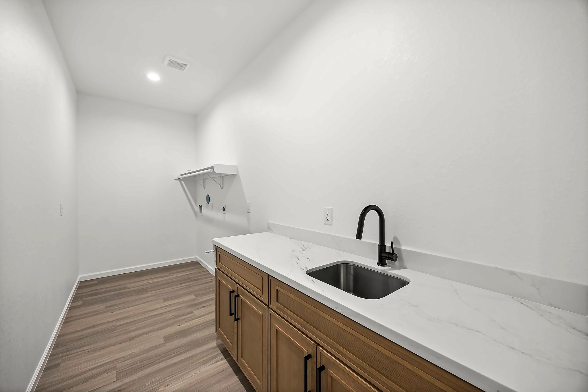 Spacious laundry room with elegant wood like flooring, modern cabinetry, and a sleek countertop featuring a built-in sink for convenience.