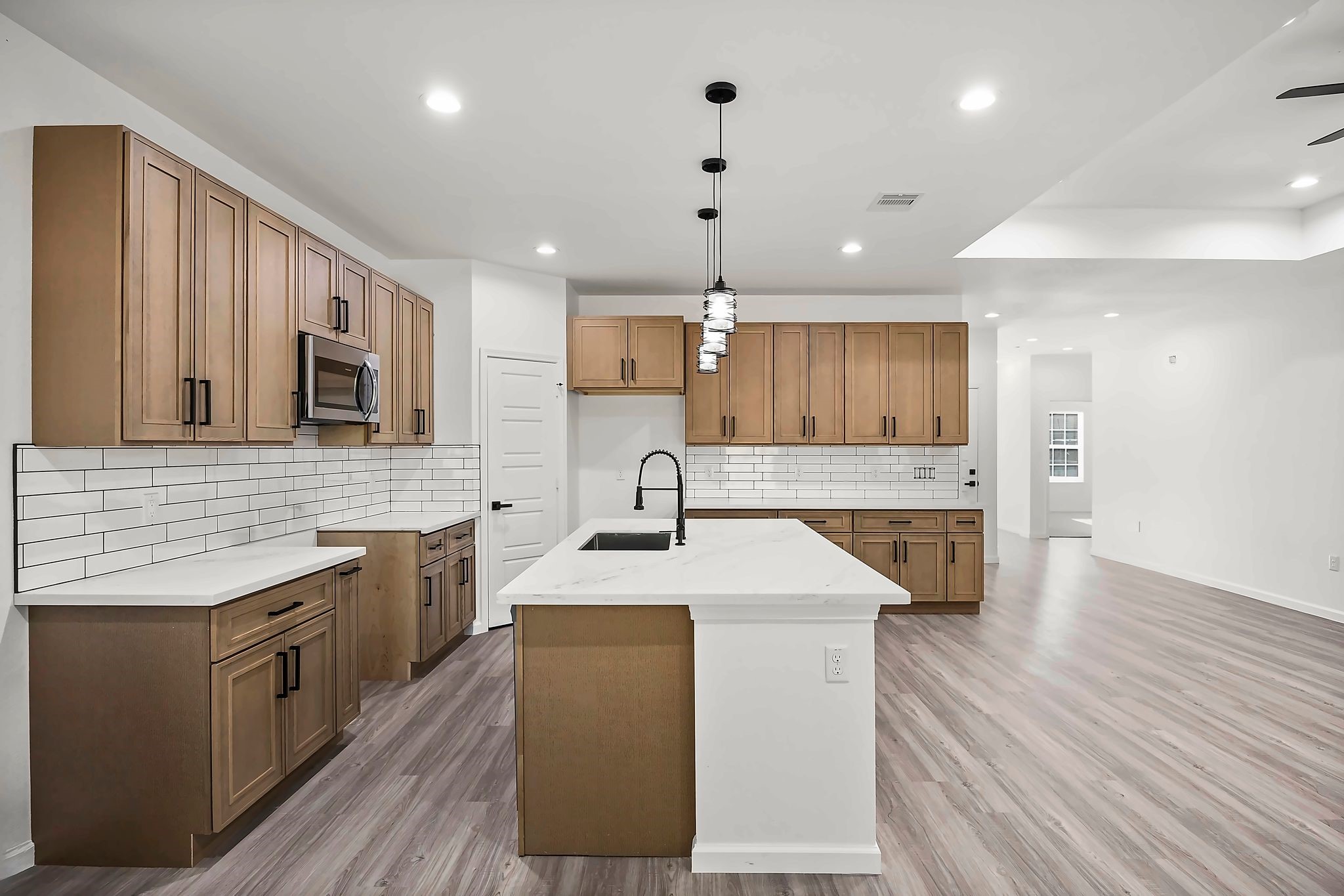 Spacious modern kitchen featuring sleek wood cabinetry, a large island with a sink, and elegant pendant lighting, complemented by a subway tile backsplash and stainless steel appliances.