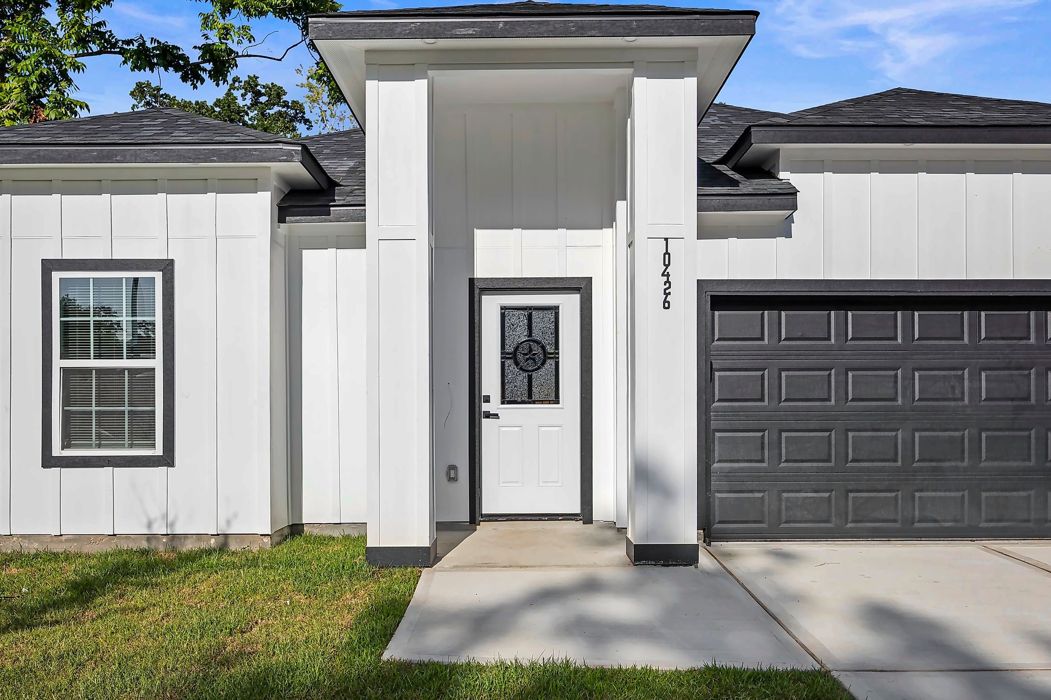 Modern white facade with sleek black accents, featuring a stylish front door and attached garage, set against a well-maintained lawn.