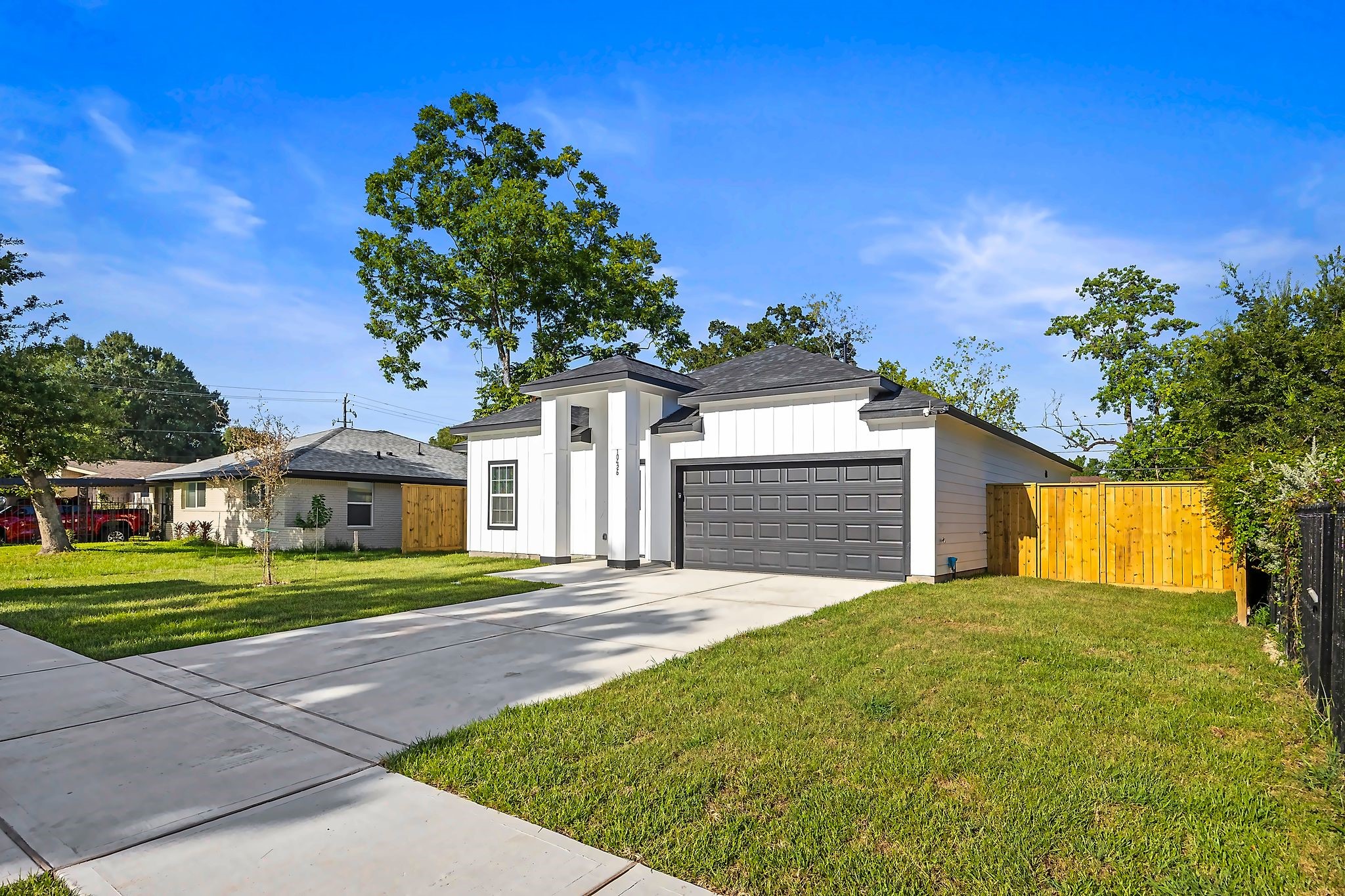 Modern single-story home with a sleek white exterior and contrasting dark garage door, set on a spacious, manicured lot with a wide driveway and fenced backyard.