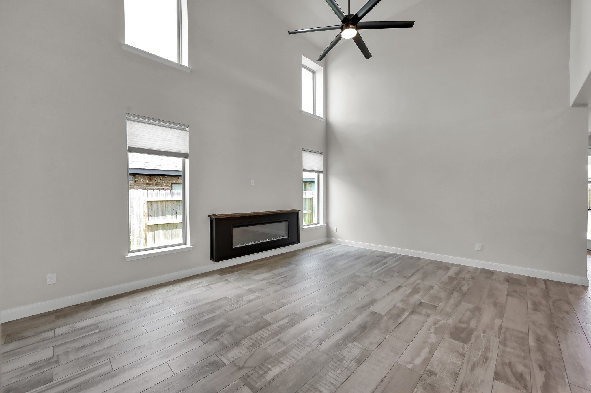 Light-filled living room with soaring ceilings, tall windows, and a sleek electric fireplace.