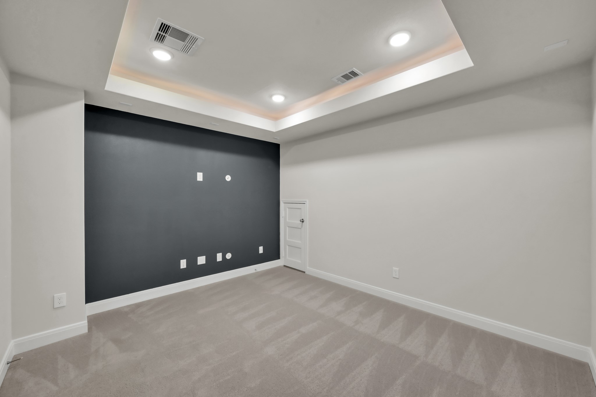 Cozy media room with tray ceiling, recessed lighting, and a bold accent wall ready for entertainment setup.