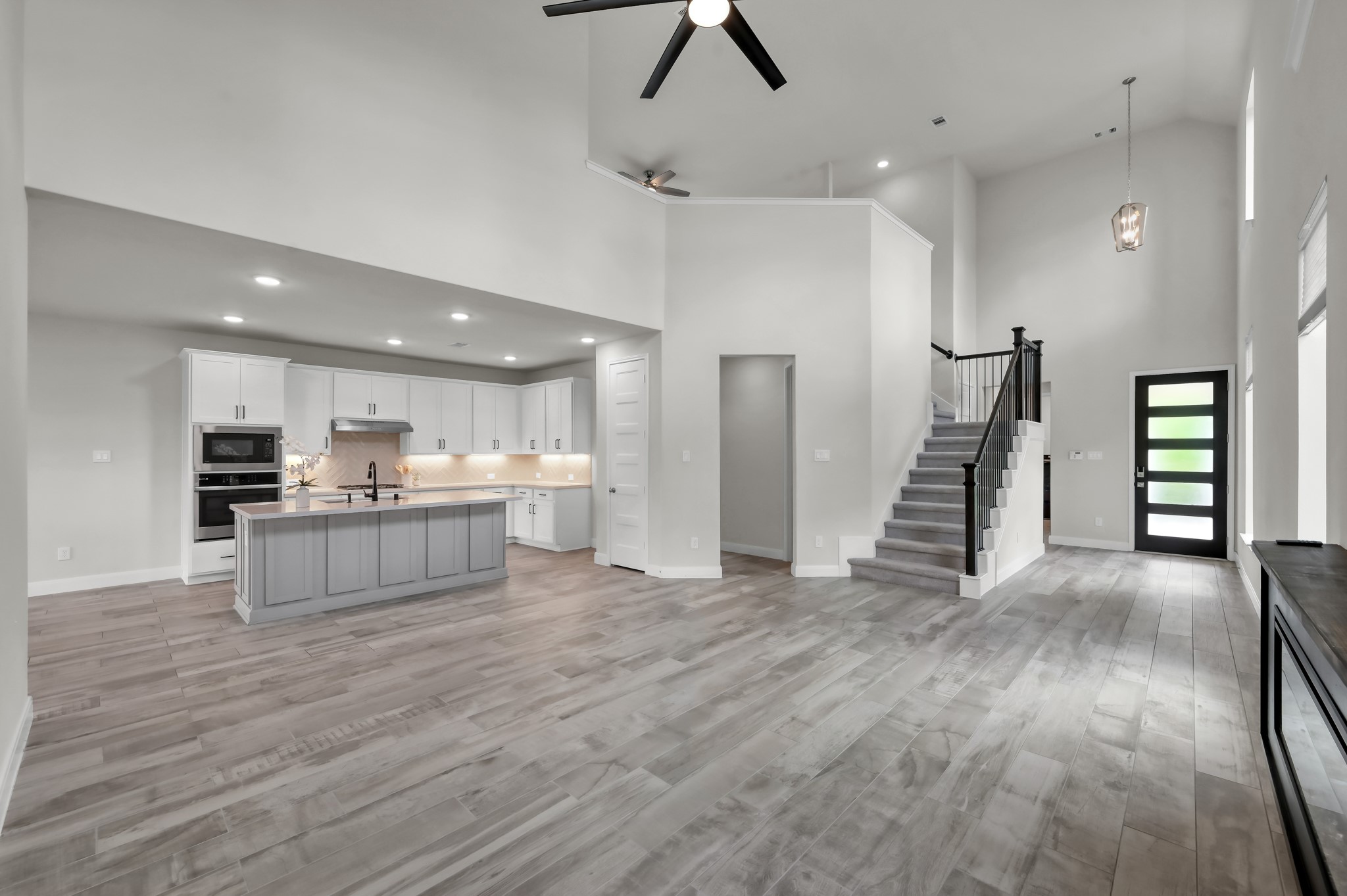 Expansive open layout with soaring ceilings, modern staircase, and seamless flow to the kitchen.