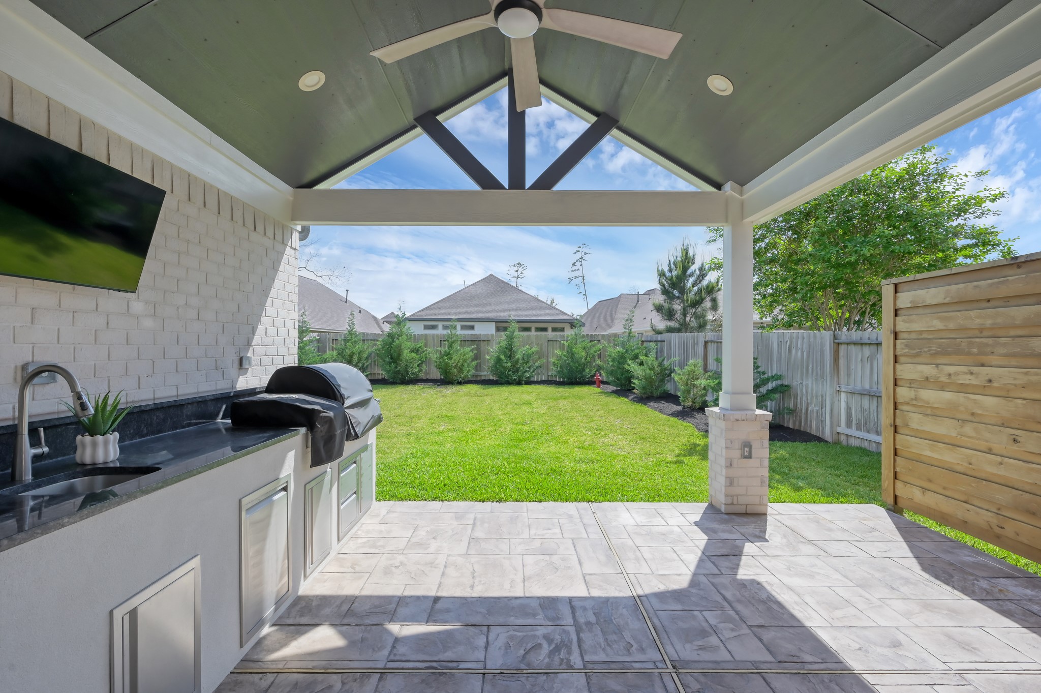 Spacious covered patio with outdoor kitchen, ceiling fan, and TV setupperfect for entertaining while enjoying the private backyard.