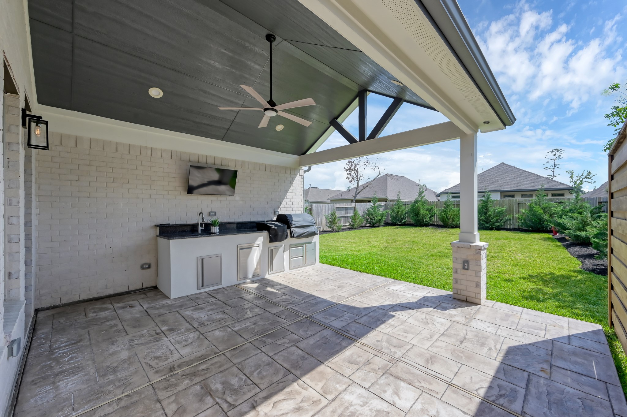 Spacious covered patio with outdoor kitchen, ceiling fan, and TV setupperfect for entertaining while enjoying the private backyard.