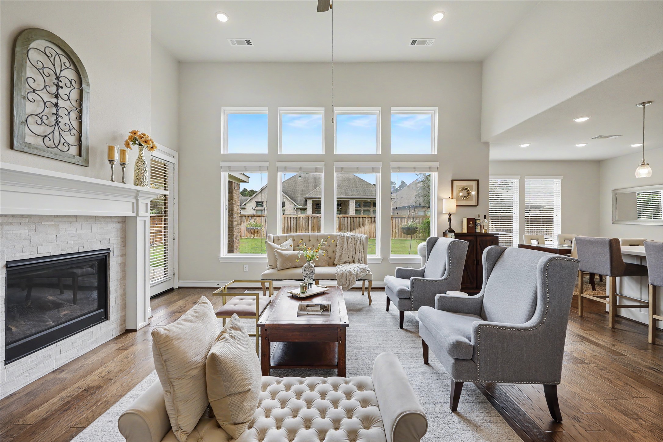 Two-story great room with fireplace, tall windows, and open sightlines to the kitchen and the backyard.