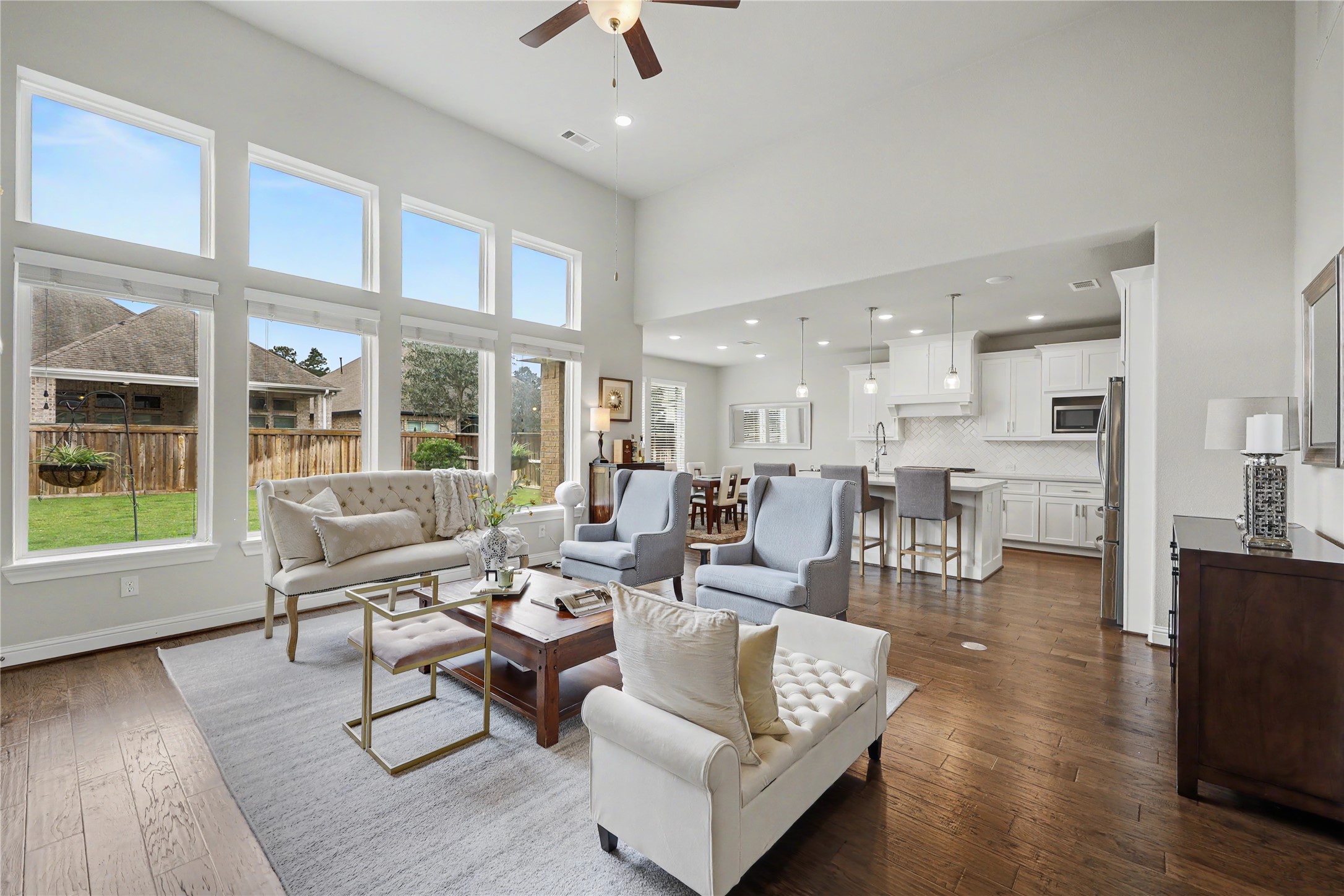 Two-story great room with soaring ceilings, fireplace, and a wall of windows overlooking the backyard.