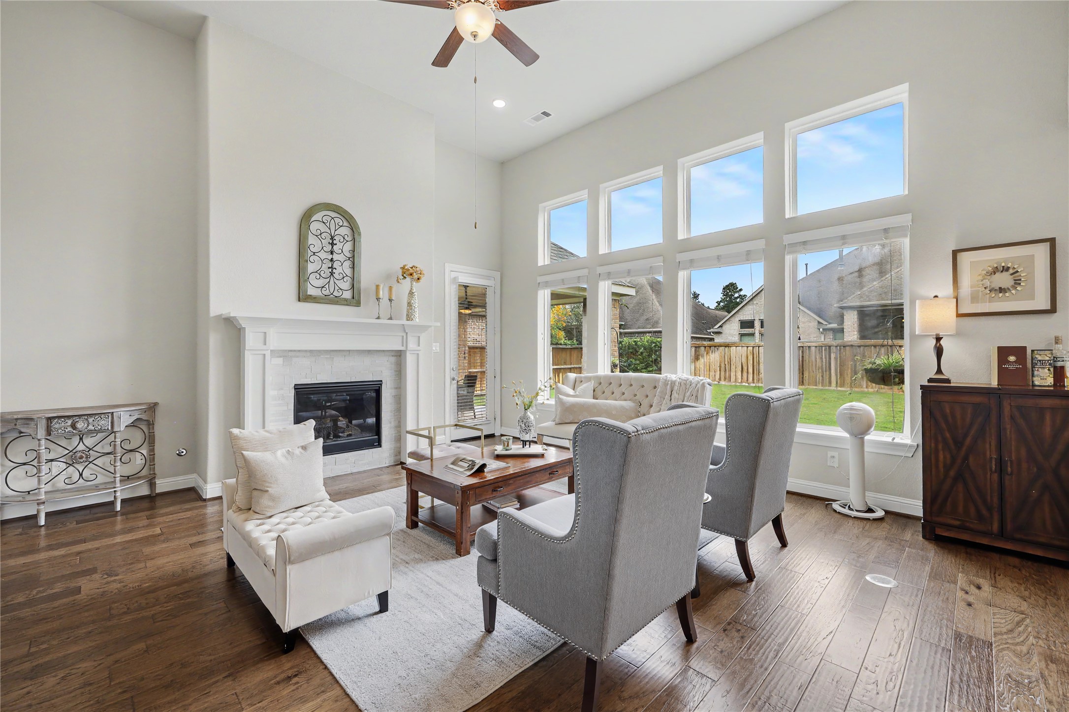 Two-story great room with fireplace, tall windows, and open sightlines to the kitchen.