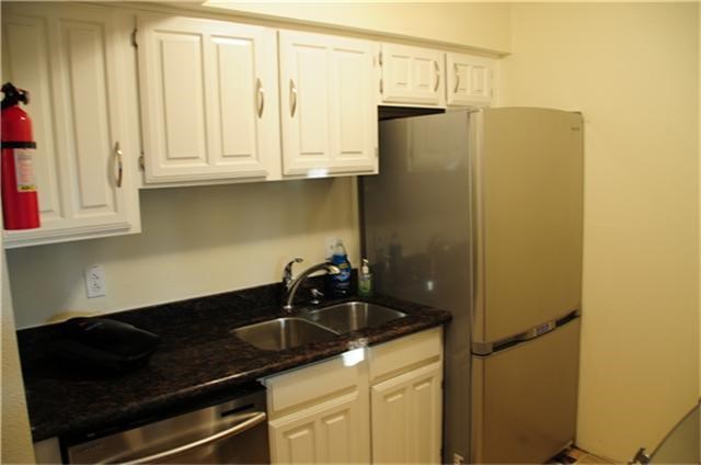 This compact kitchen features white cabinetry, a dark granite countertop, stainless steel appliances, and a sleek fridge, offering a modern and efficient space.