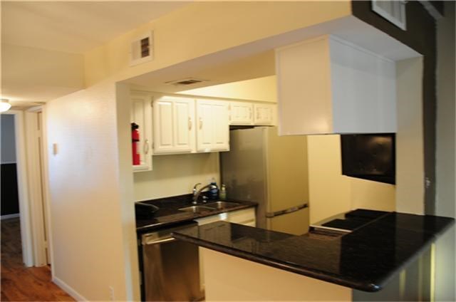 Compact kitchen with a sleek black granite countertop, stainless steel appliances, and white cabinetry. It features an open layout with a breakfast bar, creating a modern and functional space.