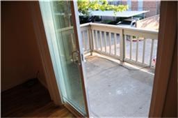 This photo shows a small balcony accessible through a sliding glass door, offering outdoor space with a railing and a view of a tree and adjacent buildings.
