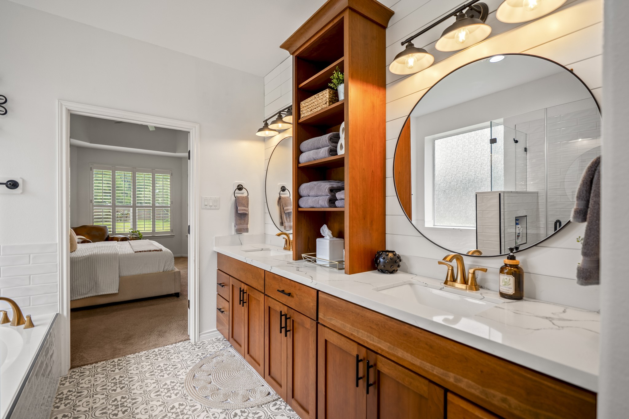 This stunning expansive dual vanity crafted from rich, warm wood cabinetry, beautifully anchored by a custom floor-to-ceiling open shelving tower for ultimate linen storage or display.