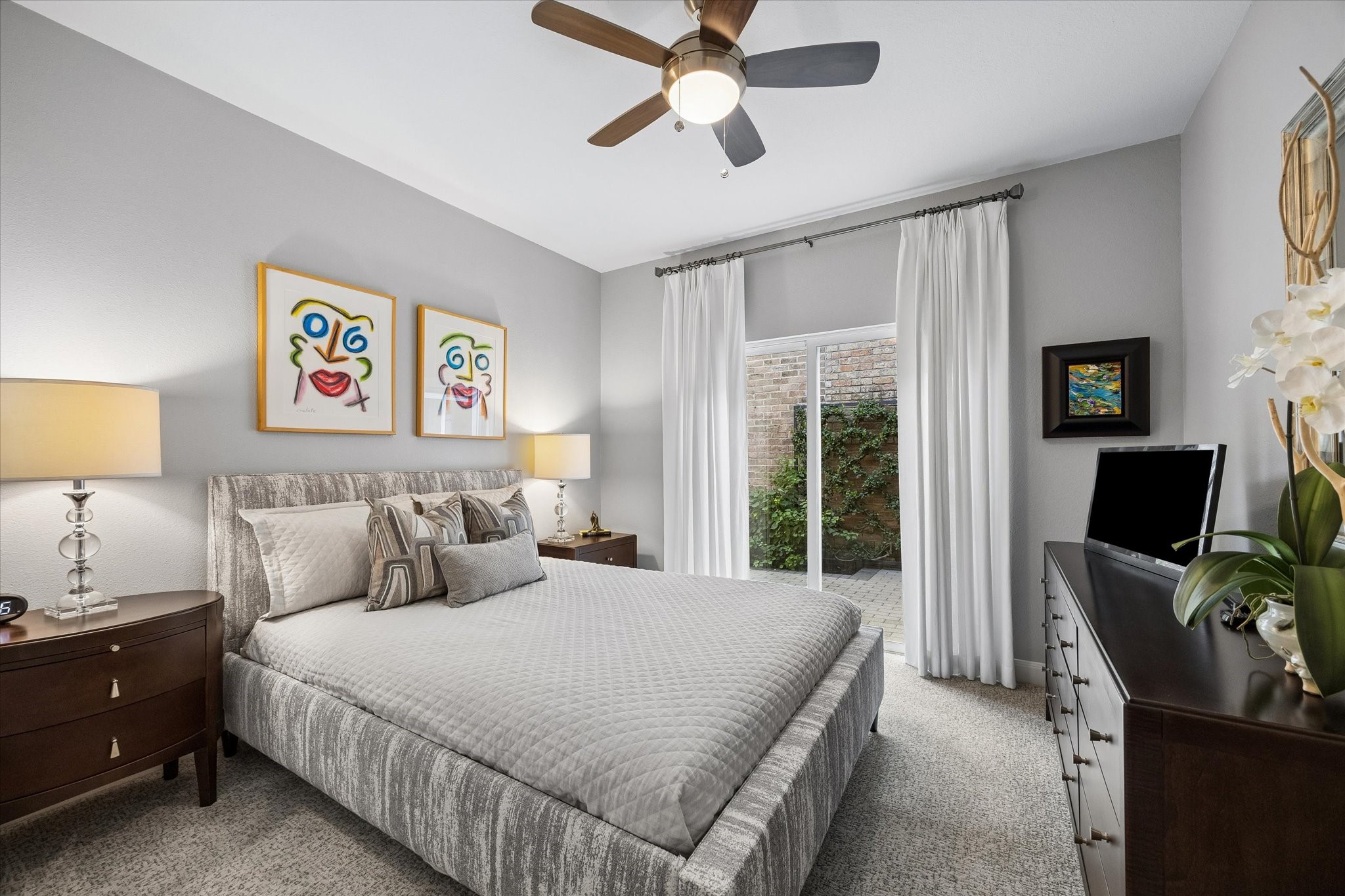 BEDROOM II: Inviting secondary bedroom offers plush carpeting, custom window treatments, a ceiling fan and sliding glass doors providing natural light and access to the outdoor patio area.