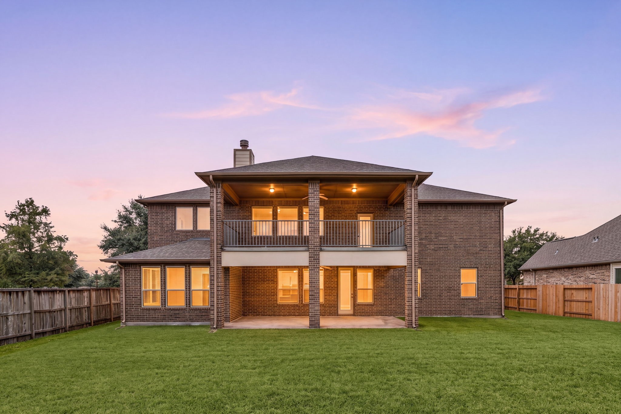Stunning twilight view showcases the homes impressive rear elevation, expansive covered second-floor deck, covered ground-level patio, and large backyardan exceptional setup for outdoor living and entertaining.