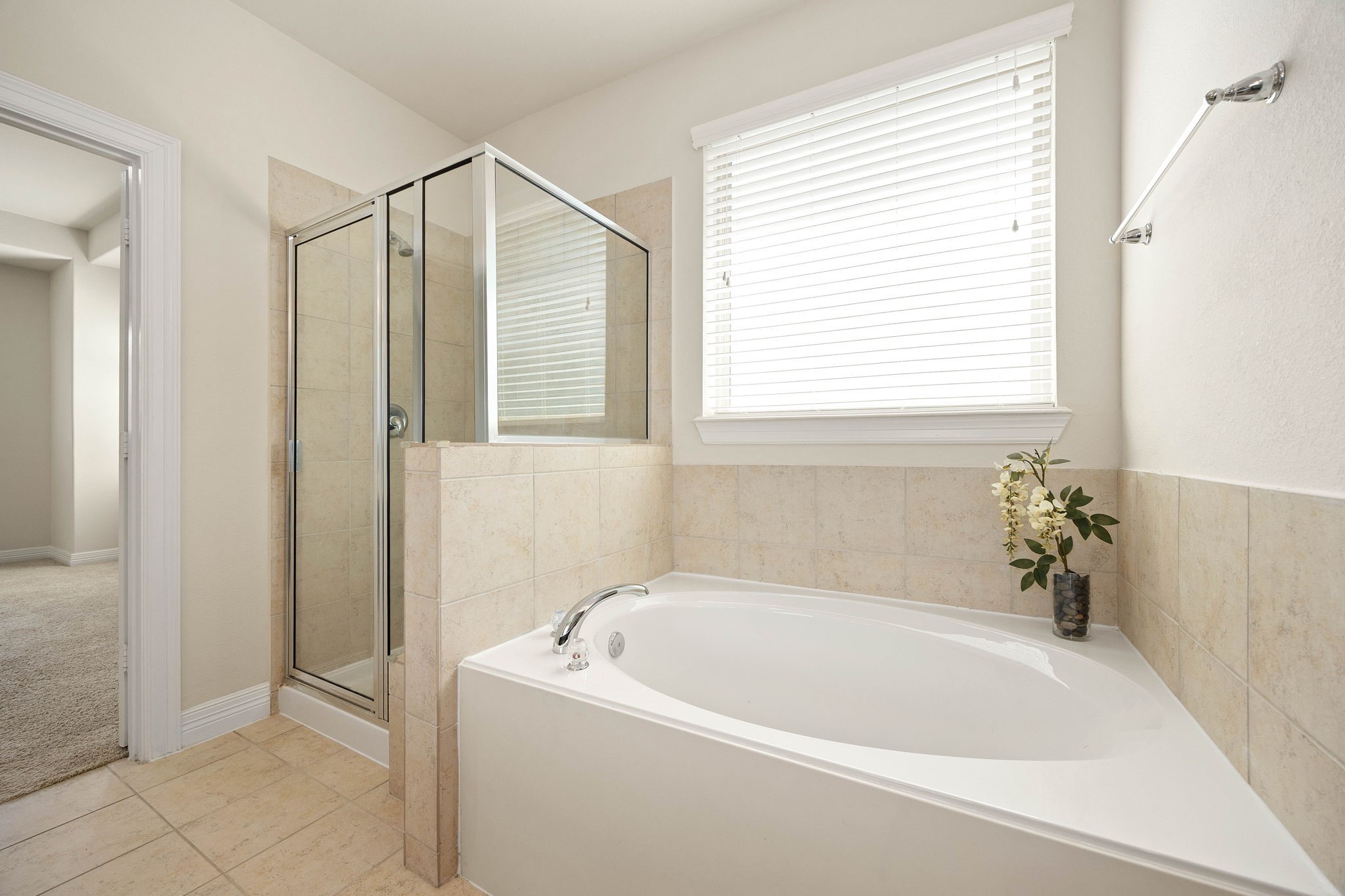 Relaxing soaking tub and separate glass-enclosed shower complete this primary bathroom with a large window providing great natural light.