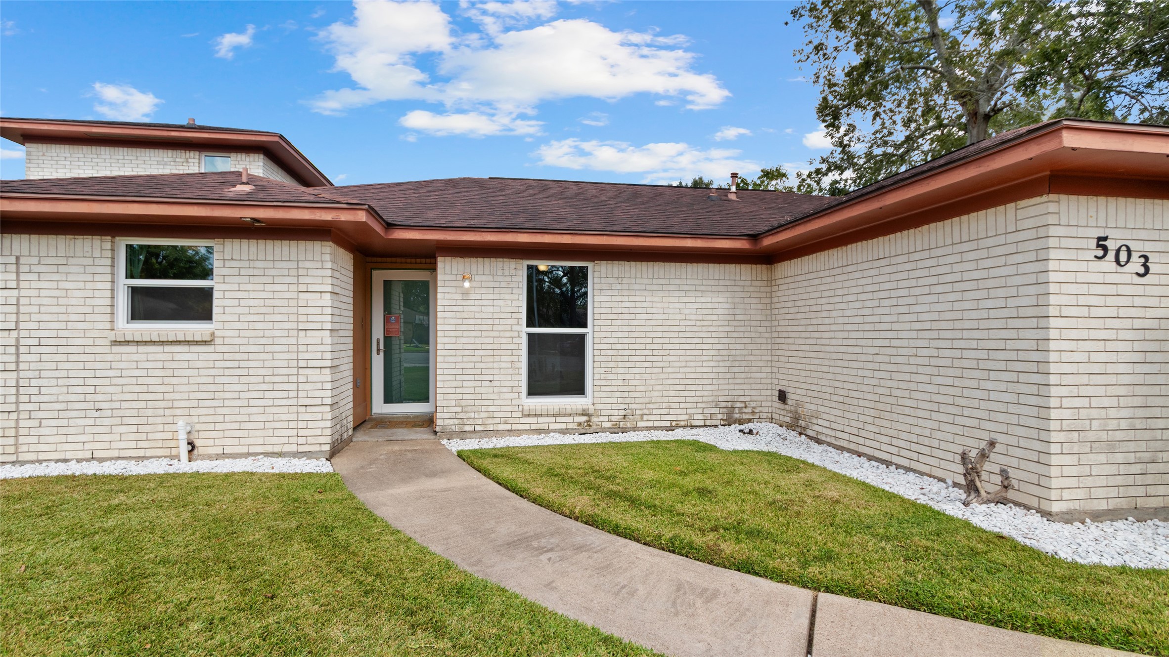 Closer exterior view highlights the home's classic brick exterior, updated windows, curved walkway, and low-maintenance landscaping leading to the front entry.