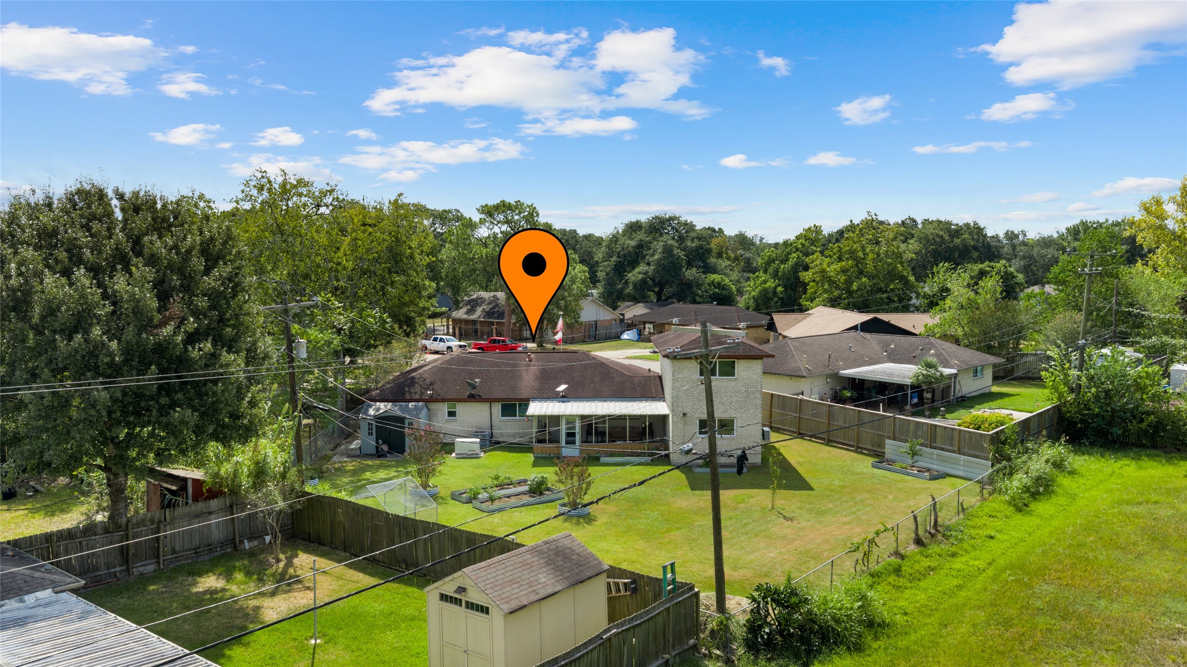 Aerial view showcases the homes expansive backyard with plenty of open green space, raised garden beds, storage shed, and covered screened patio.