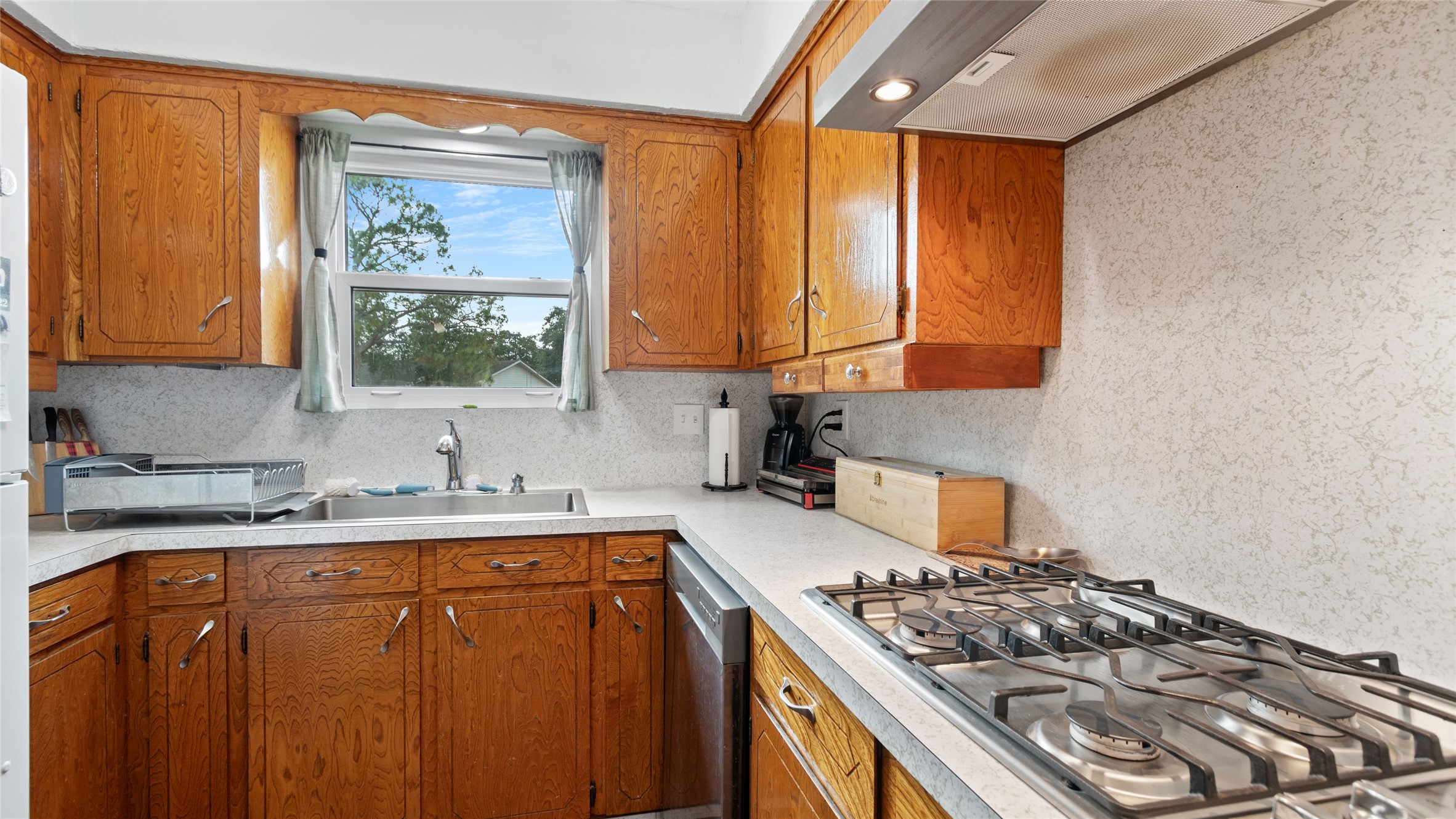 Kitchen features abundant cabinetry and counter space, a gas cooktop, stainless steel dishwasher, and a window above the sink providing natural light.