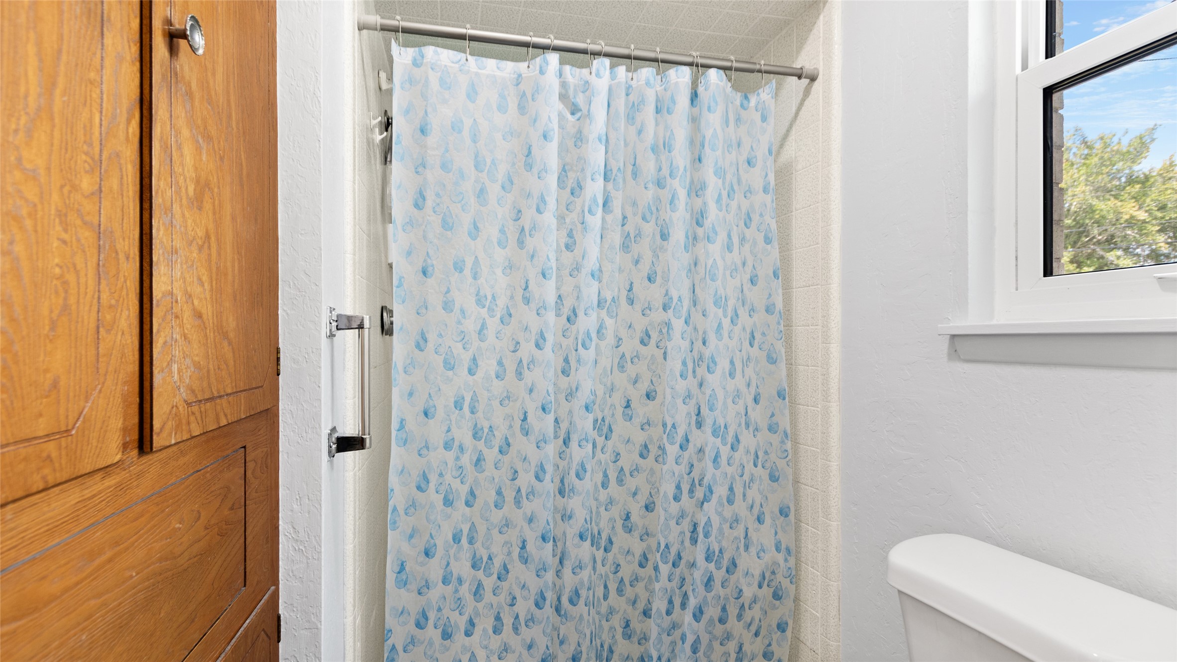 Tub/shower combination with tiled surround and a nearby window bringing natural light into the full bathroom.