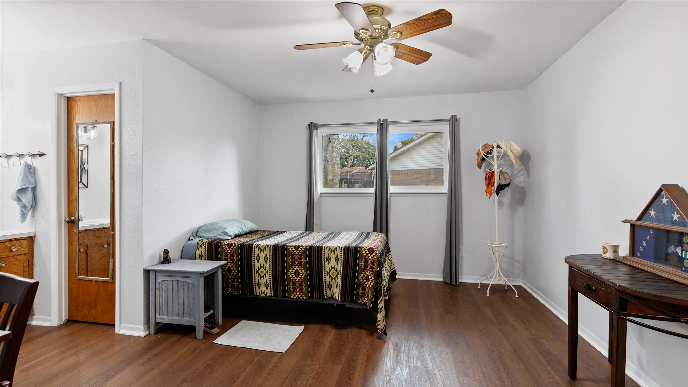 Generously sized bedroom features wood-look flooring, a ceiling fan, ample wall space, and convenient access to the adjoining bath.