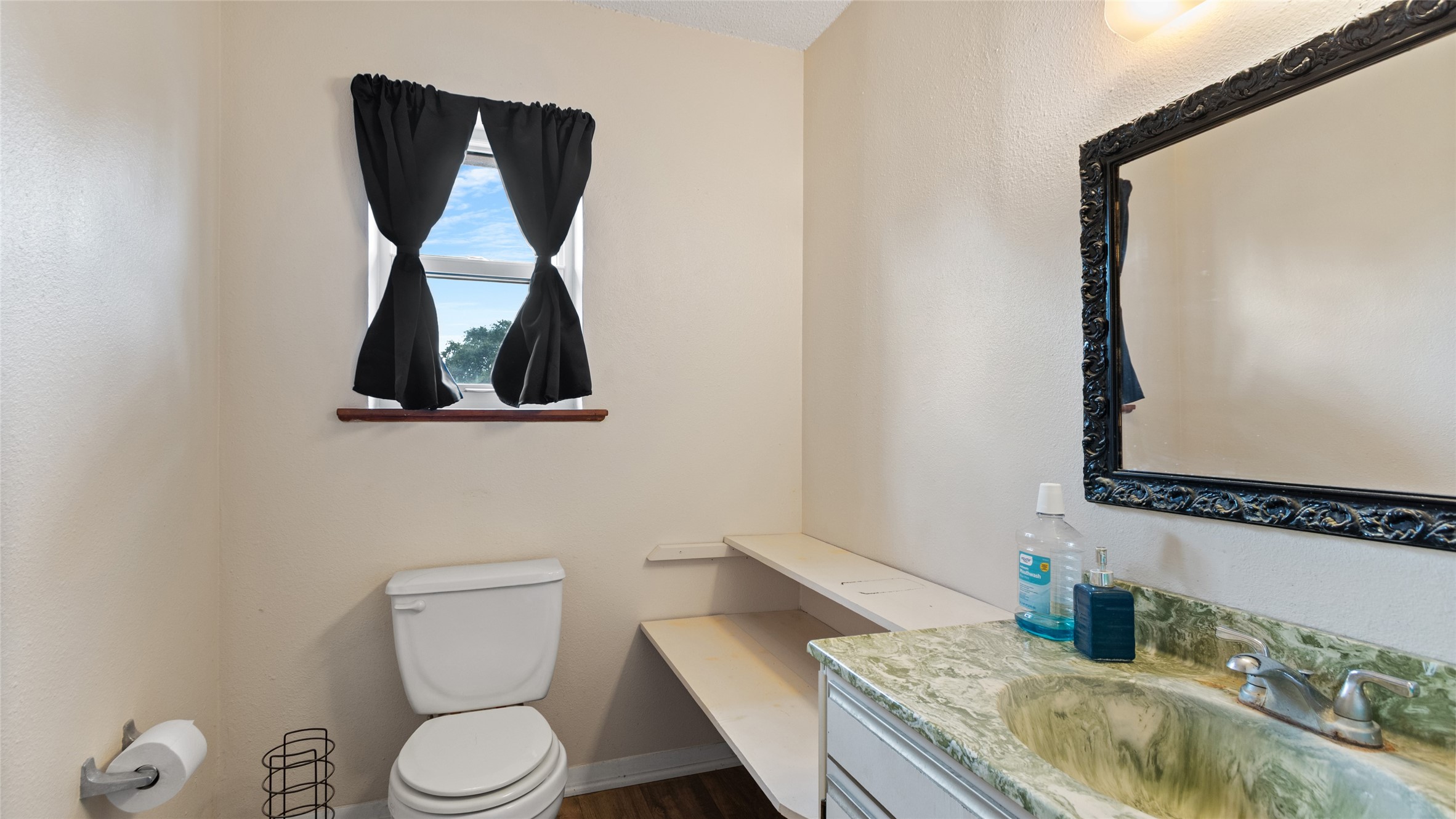 Another view of the private bath, featuring a vanity with generous counter space, built-in open shelving for convenient storage, and a window for natural light.
