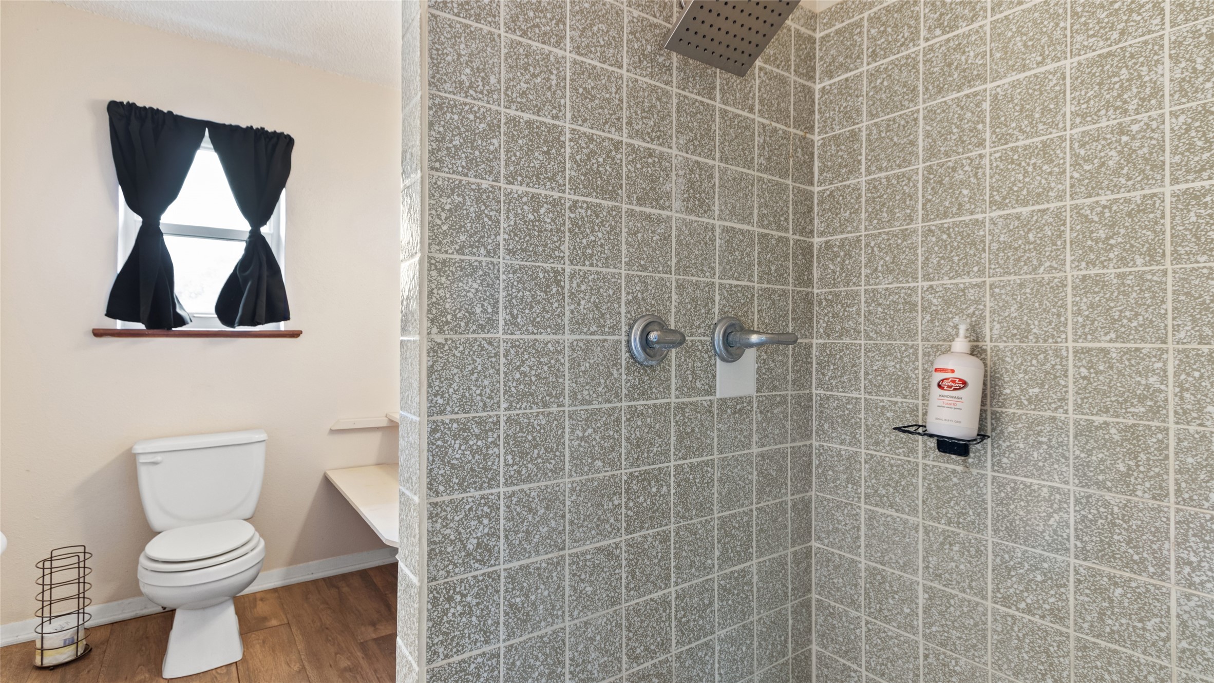 Private bath featuring a tiled walk-in shower with rainfall showerhead and a window providing natural light.