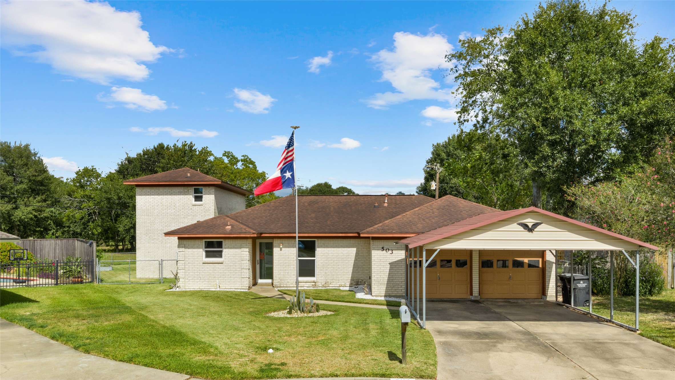 Charming brick home with a welcoming front lawn, attached two-car garage, additional covered parking, and gated access to the backyard.