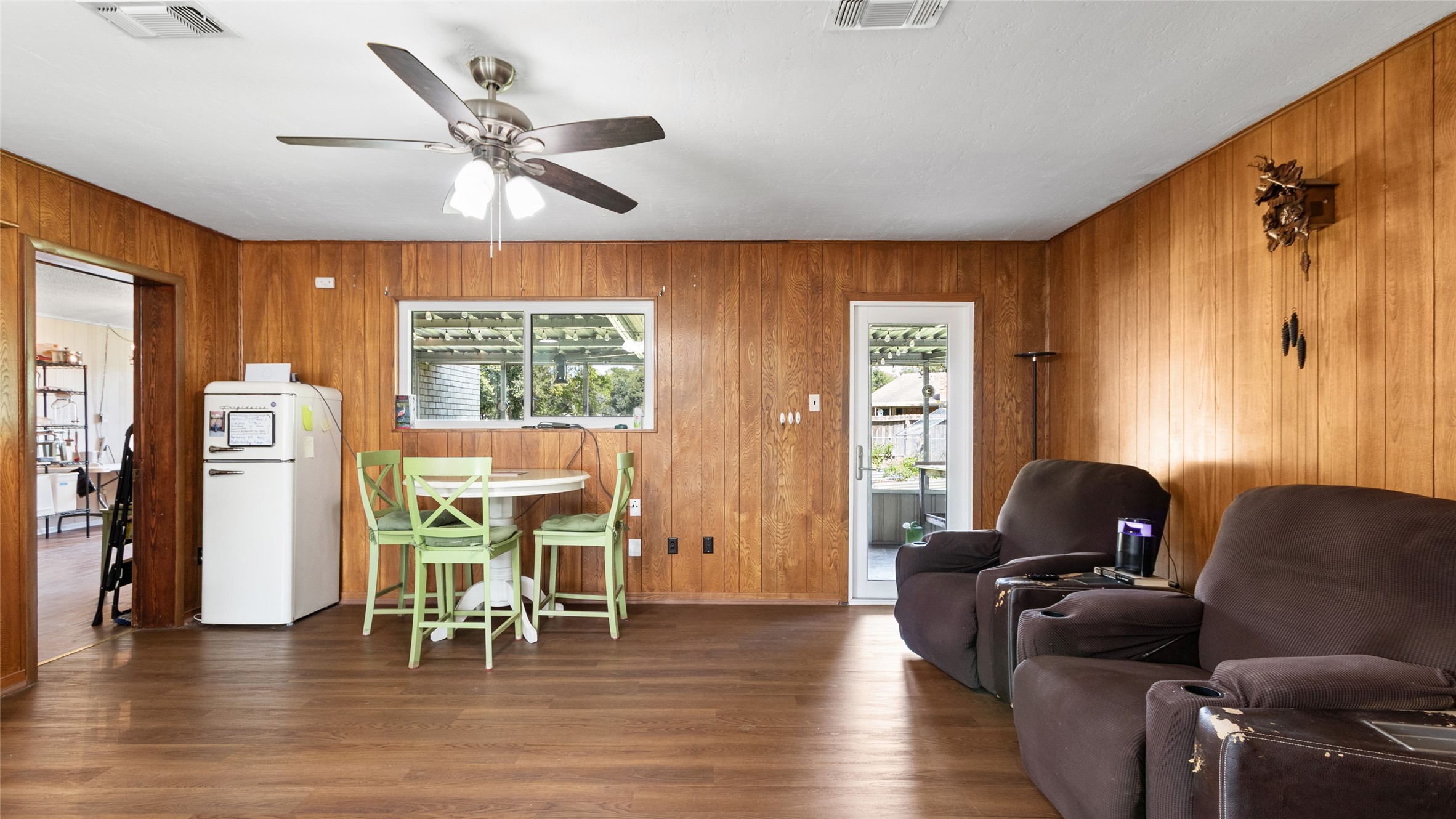 Generously sized living area features wood-look flooring, a ceiling fan, and direct access to the covered outdoor space and backyard.