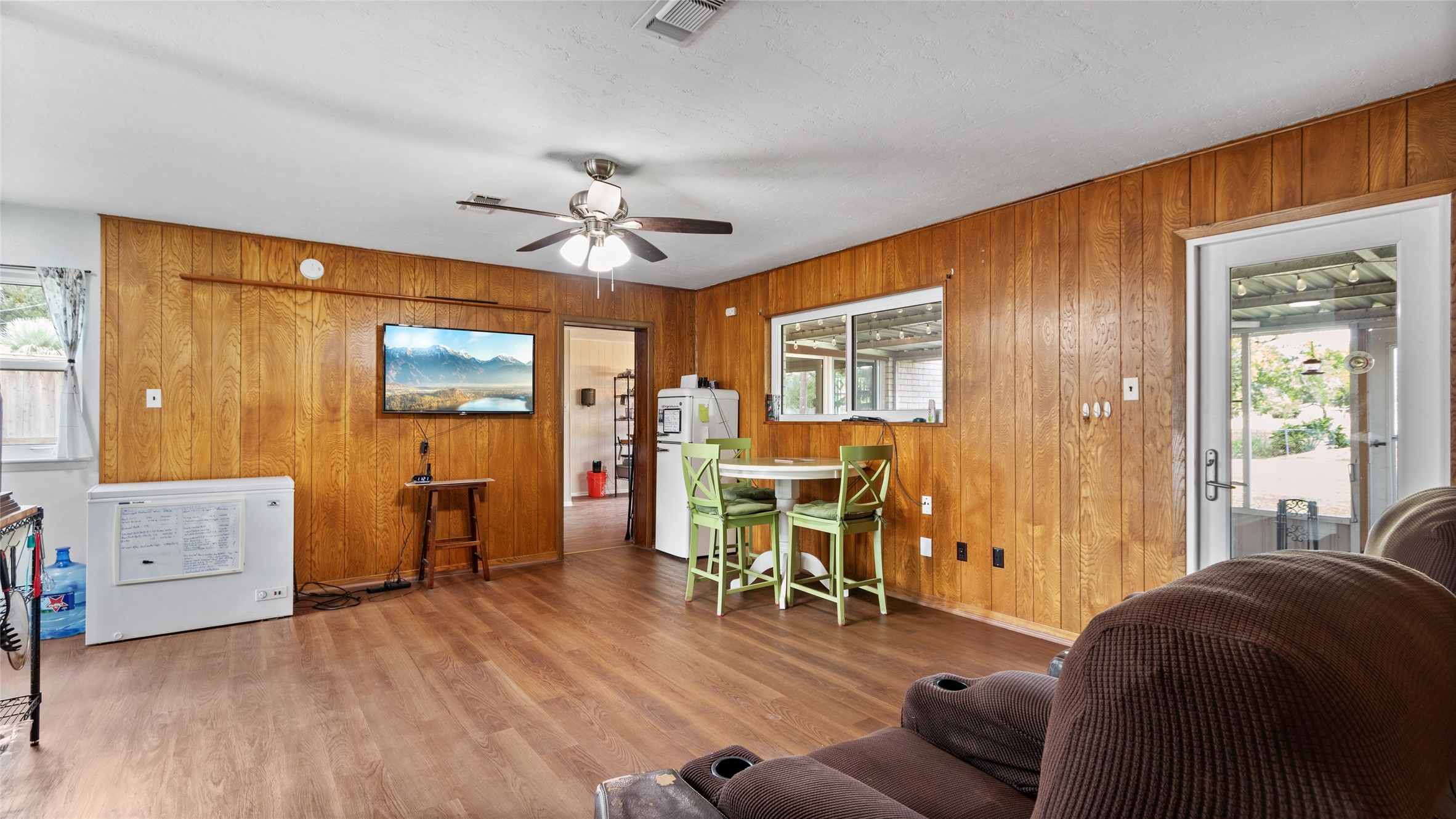 Alternate view of the living area highlights its generous proportions, durable wood-look flooring, abundant natural light, and easy access to the covered outdoor living space.
