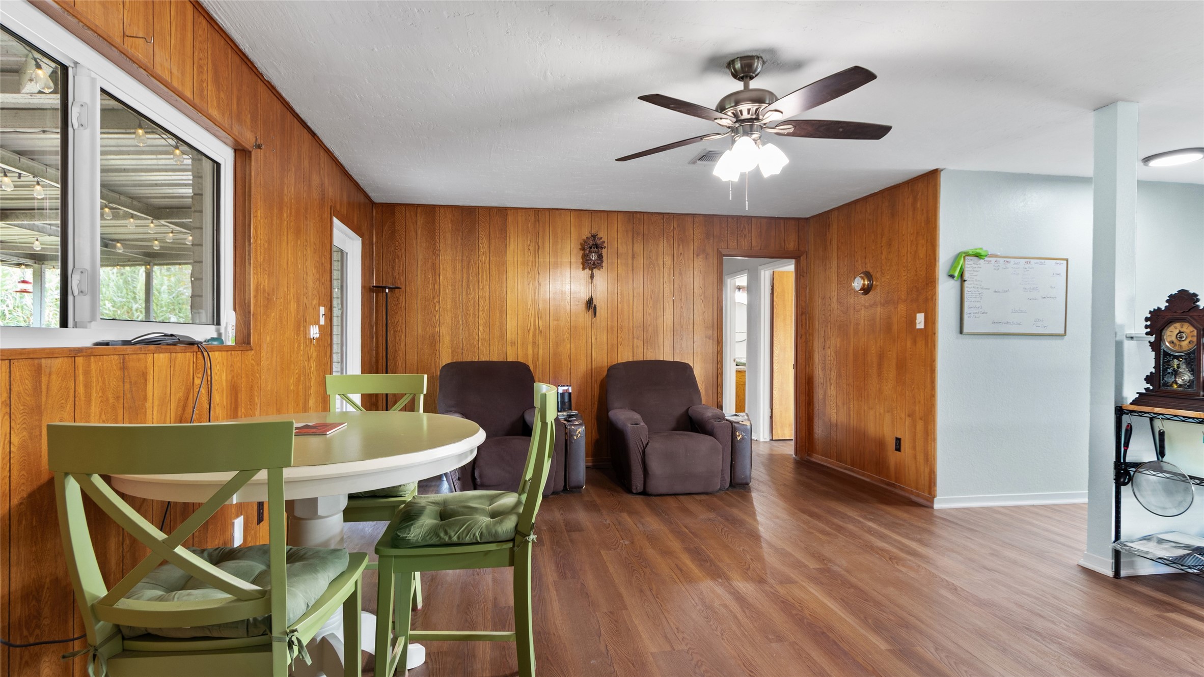 Additional view highlights the versatile living space, wood-look flooring, ceiling fan, and large interior window connecting the room visually to the covered outdoor area.