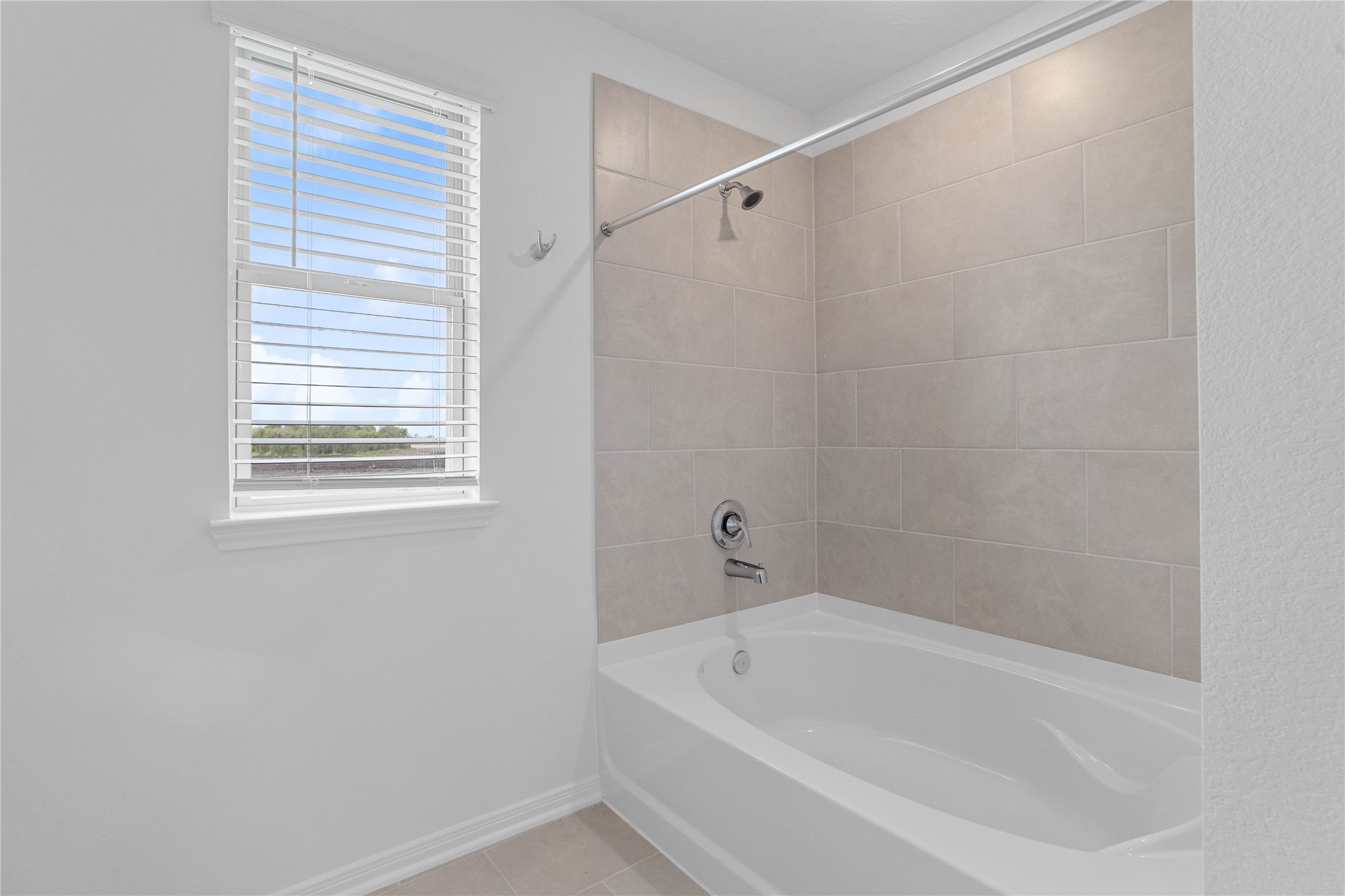 This additional view of the primary bath highlights an oversized tub/shower combination with tile surround, and a large window with blinds that offers both natural light and privacy.