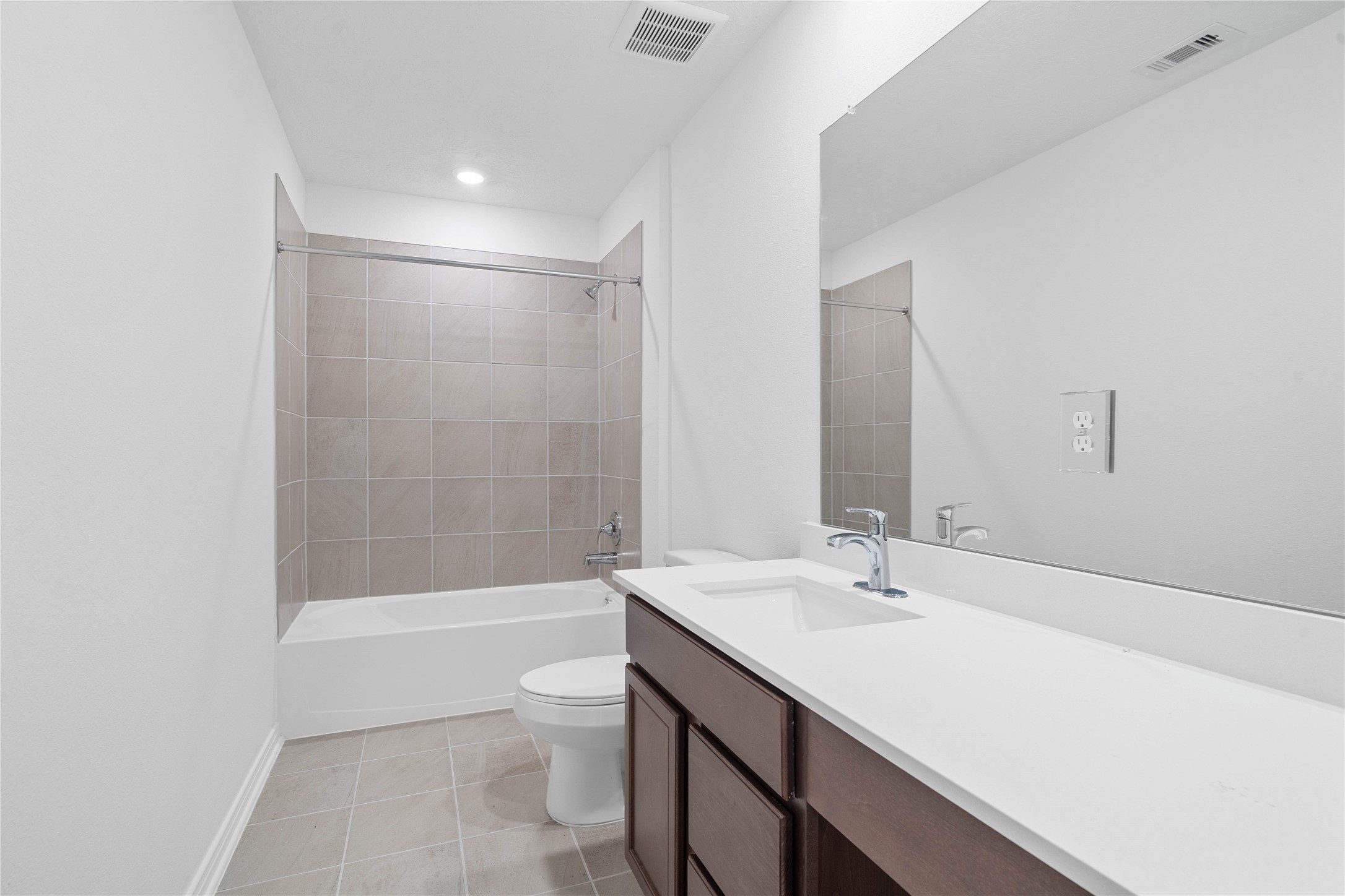 The secondary bathroom showcases tile flooring, a bath/shower combo with Daltile tile surround, a vanity with knee space and stunning light countertop, a mirror, sleek fixtures, and contemporary finishes throughout.