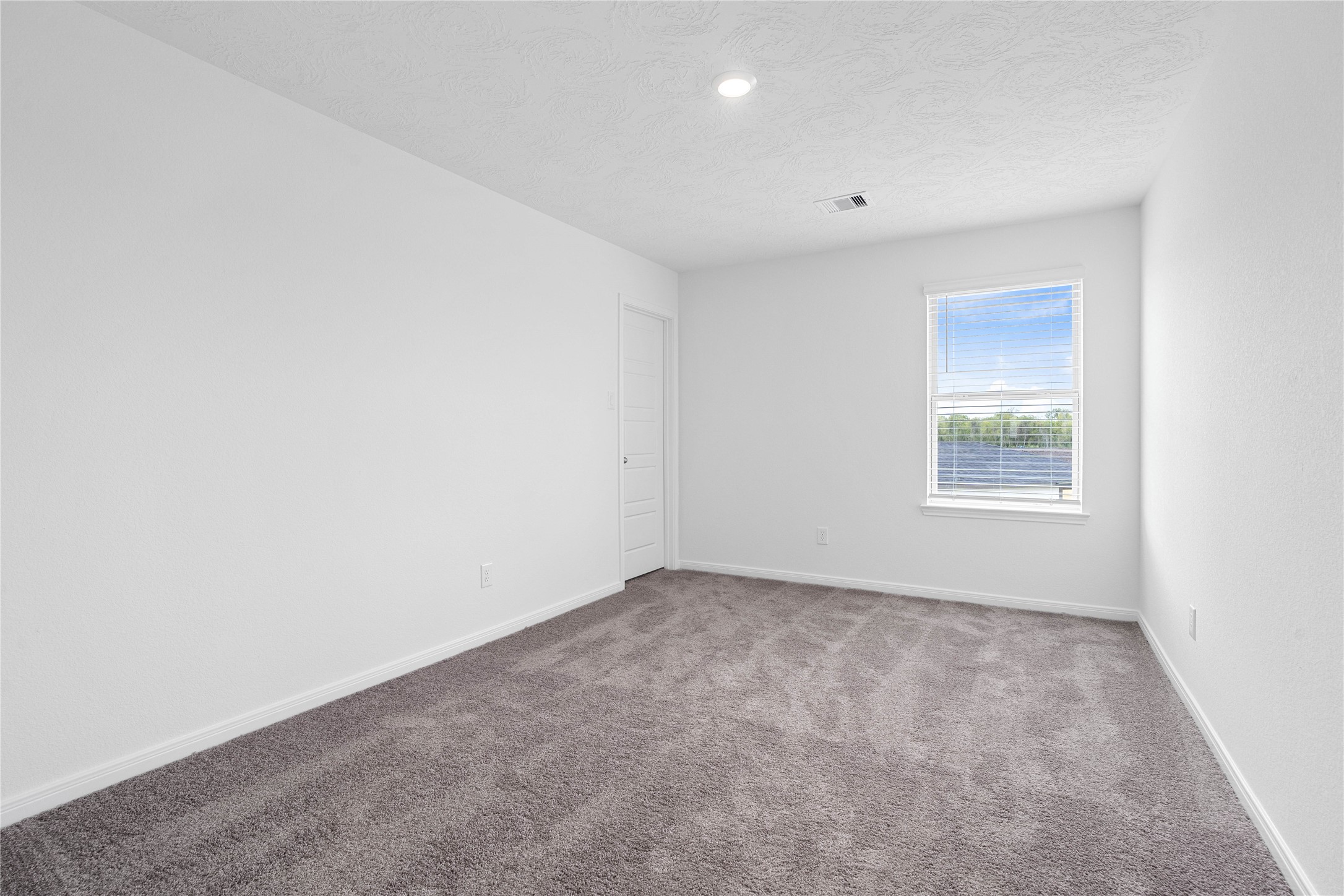 This secondary bedroom offers comfort and style with plush carpeting, neutral paint tones, recessed lighting, a large window with blinds, and a walk-in closet.